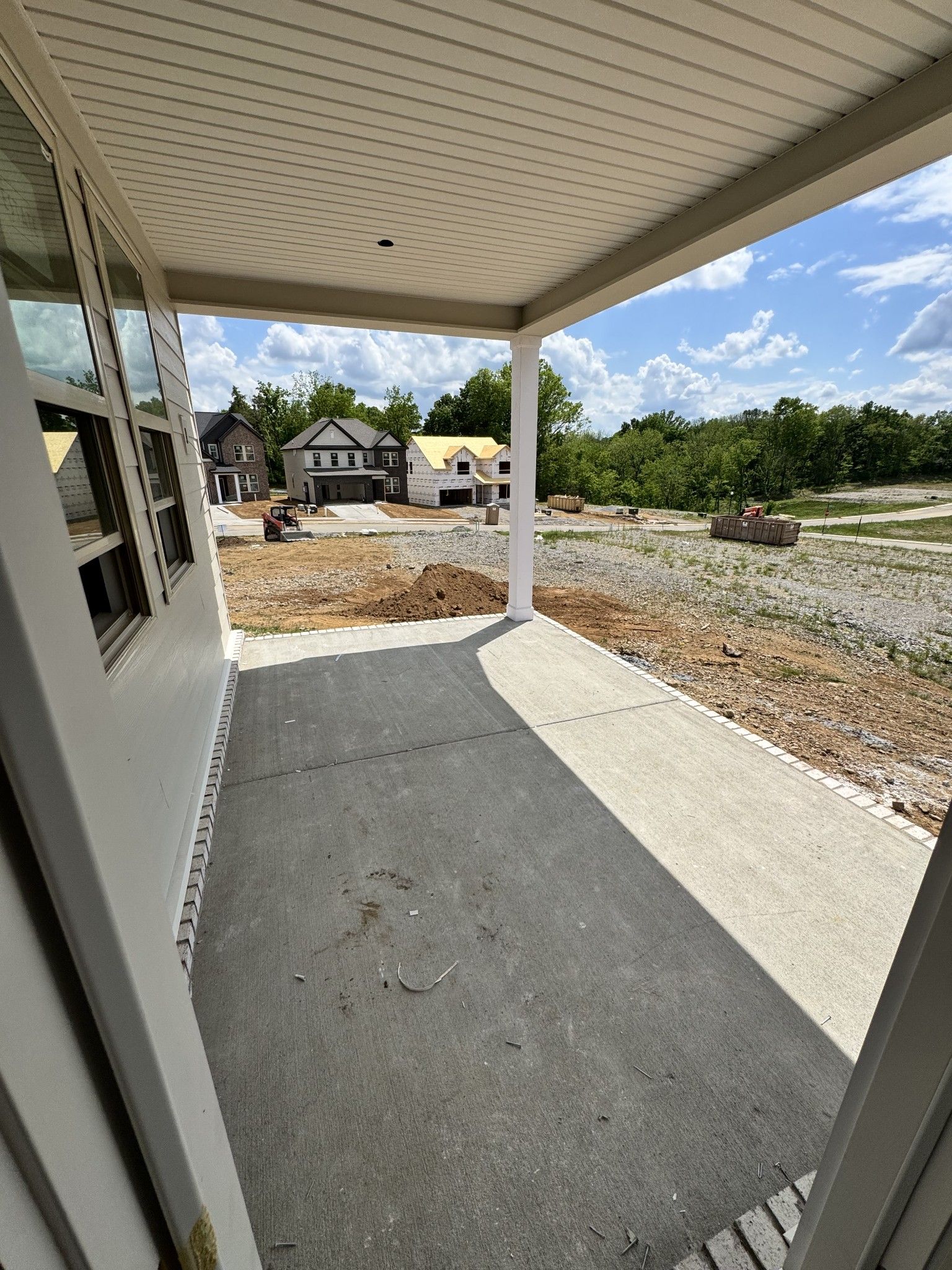Covered front porch with board-and-batten siding, large windows, and concrete slab overlooking new construction in Woods Crossing, Gallatin, TN