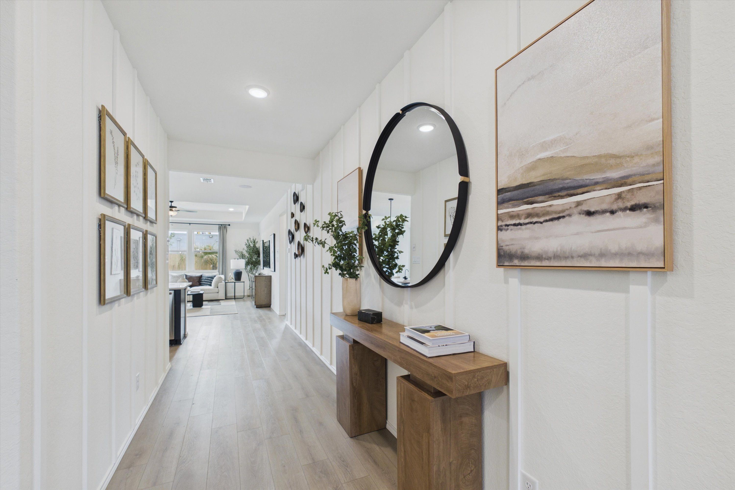Elegant shiplap hallway in Rayburn Valley San Antonio TX home by Davidson Homes featuring light oak floors, wooden console table, round black mirror and abstract art