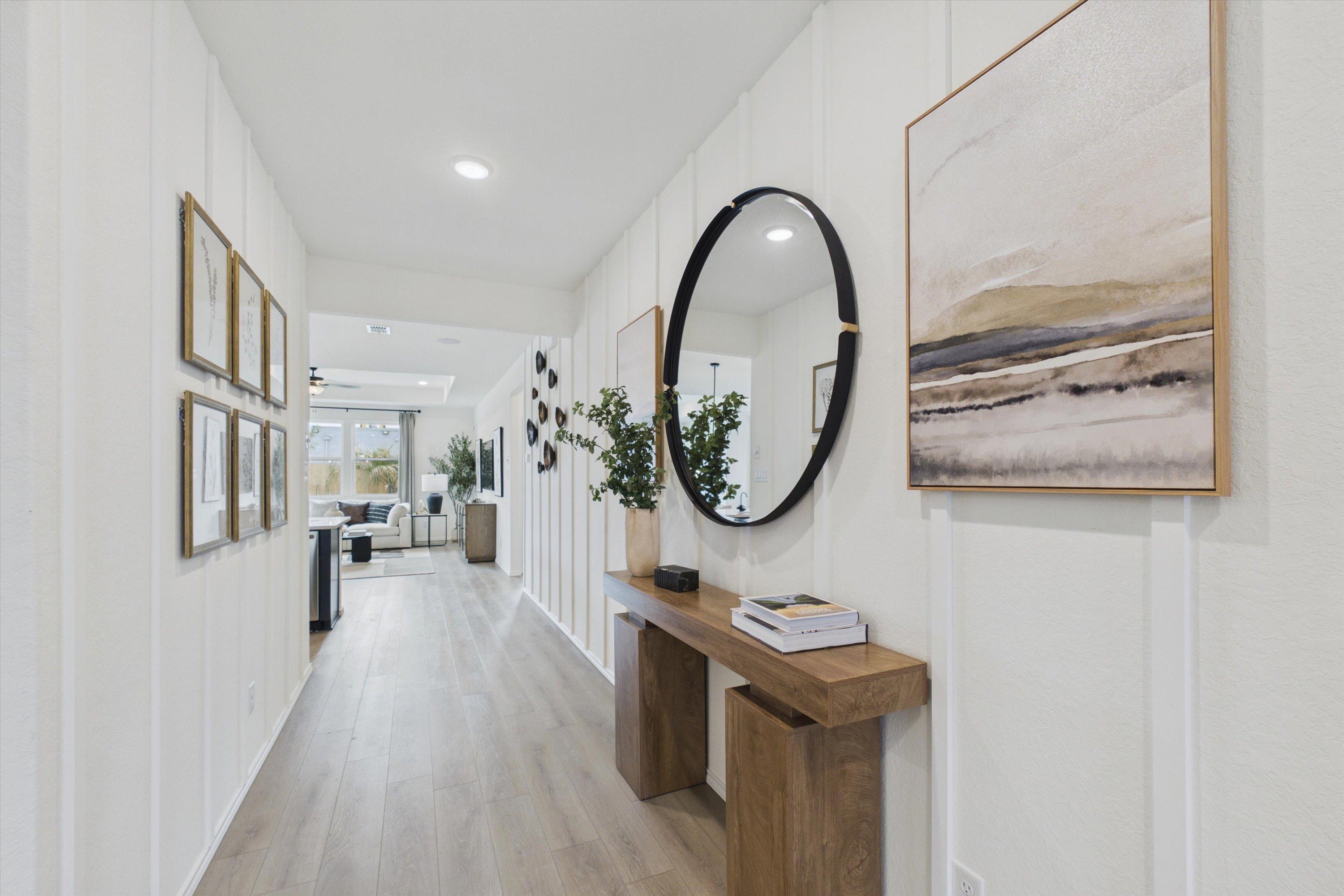 Elegant shiplap hallway in Rayburn Valley San Antonio TX home by Davidson Homes featuring light oak floors, wooden console table, round black mirror and abstract art