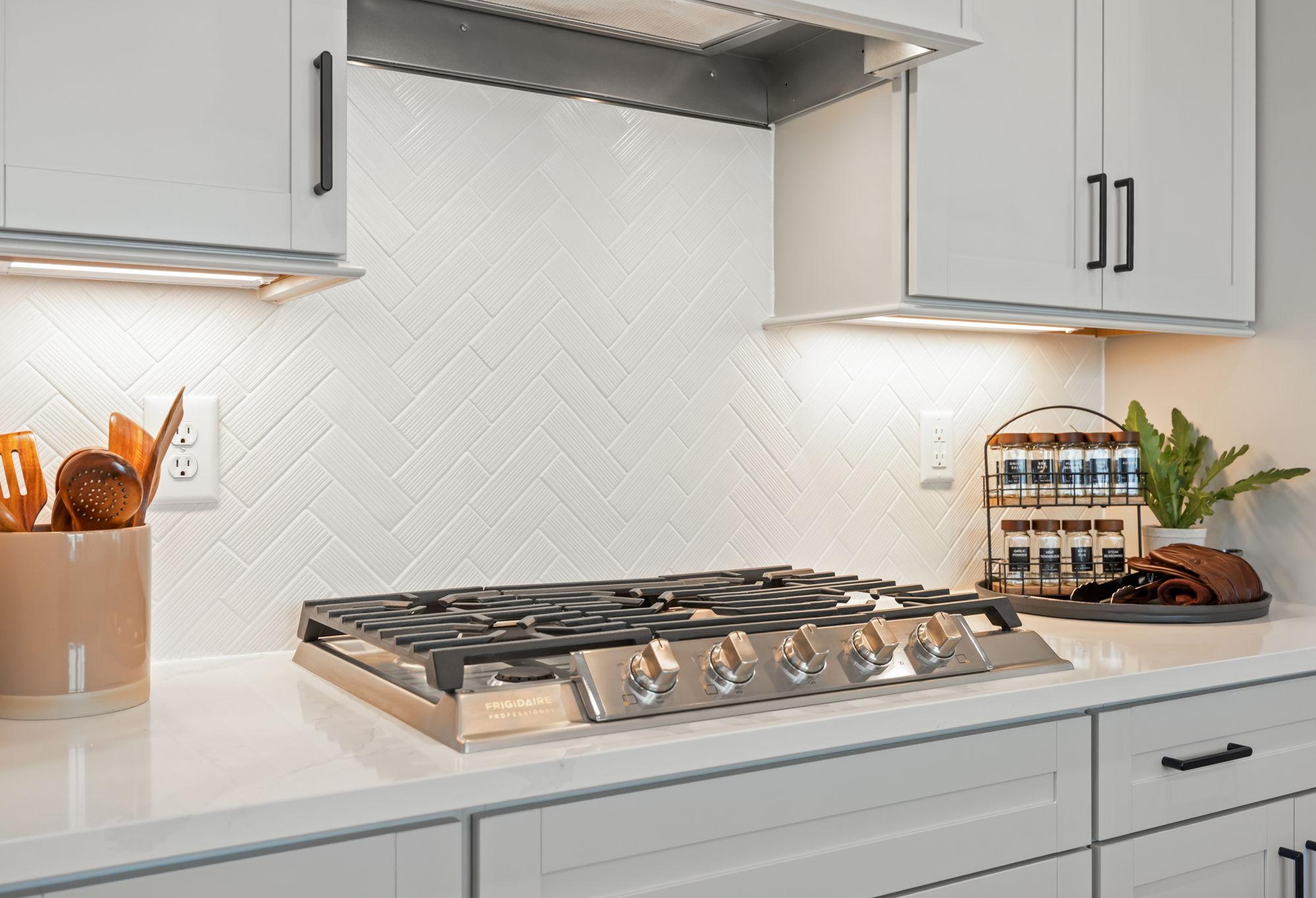 Modern kitchen in The Mitchell featuring a stainless steel gas cooktop, white herringbone backsplash, and quartz counters.