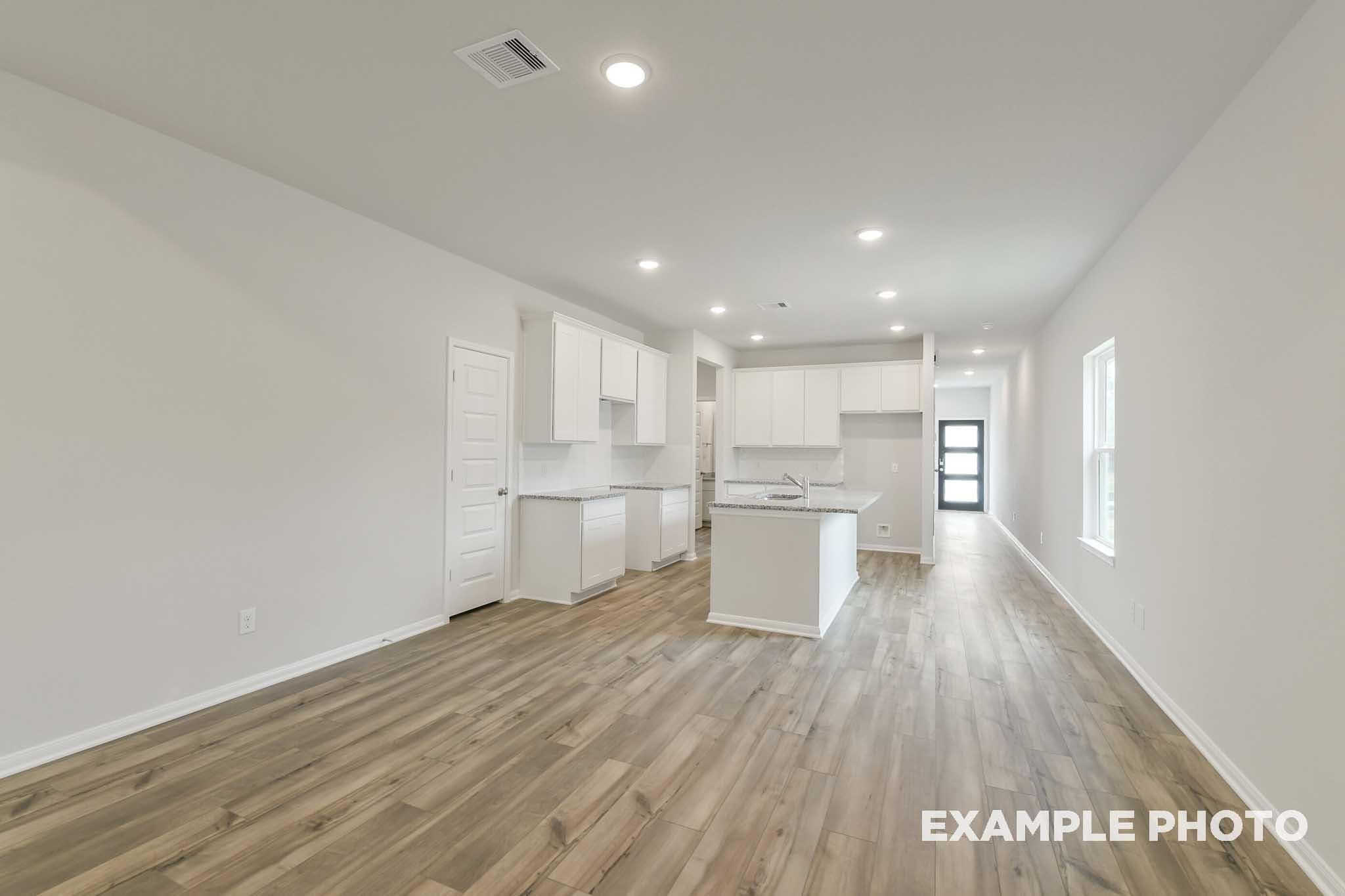 Open-concept kitchen and living area in The Frio floor plan featuring white cabinetry, granite countertops, and wood flooring.