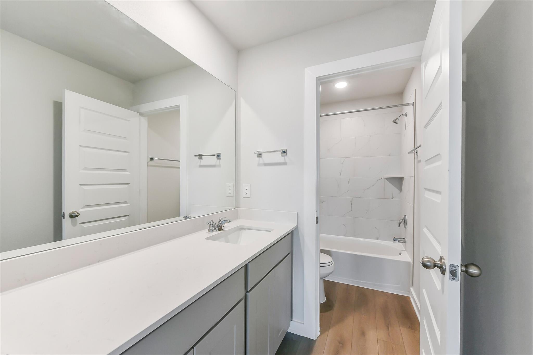 Bright bathroom with white vanity, single sink, bathtub-shower combo, and tiled walls in Davidson Homes The Brazos E, Magnolia, Texas