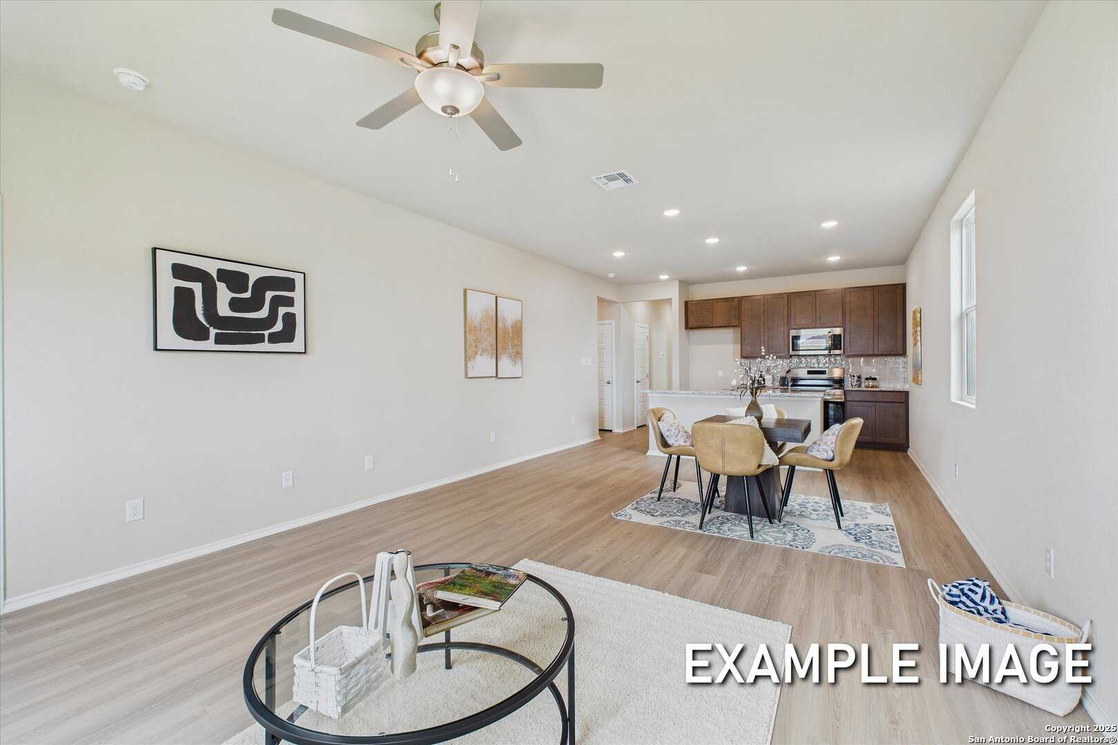 Open-concept living-dining area with ceiling fan, wooden table, chairs, and kitchen cabinets in Davidson Homes The Comal B, Agave San Antonio