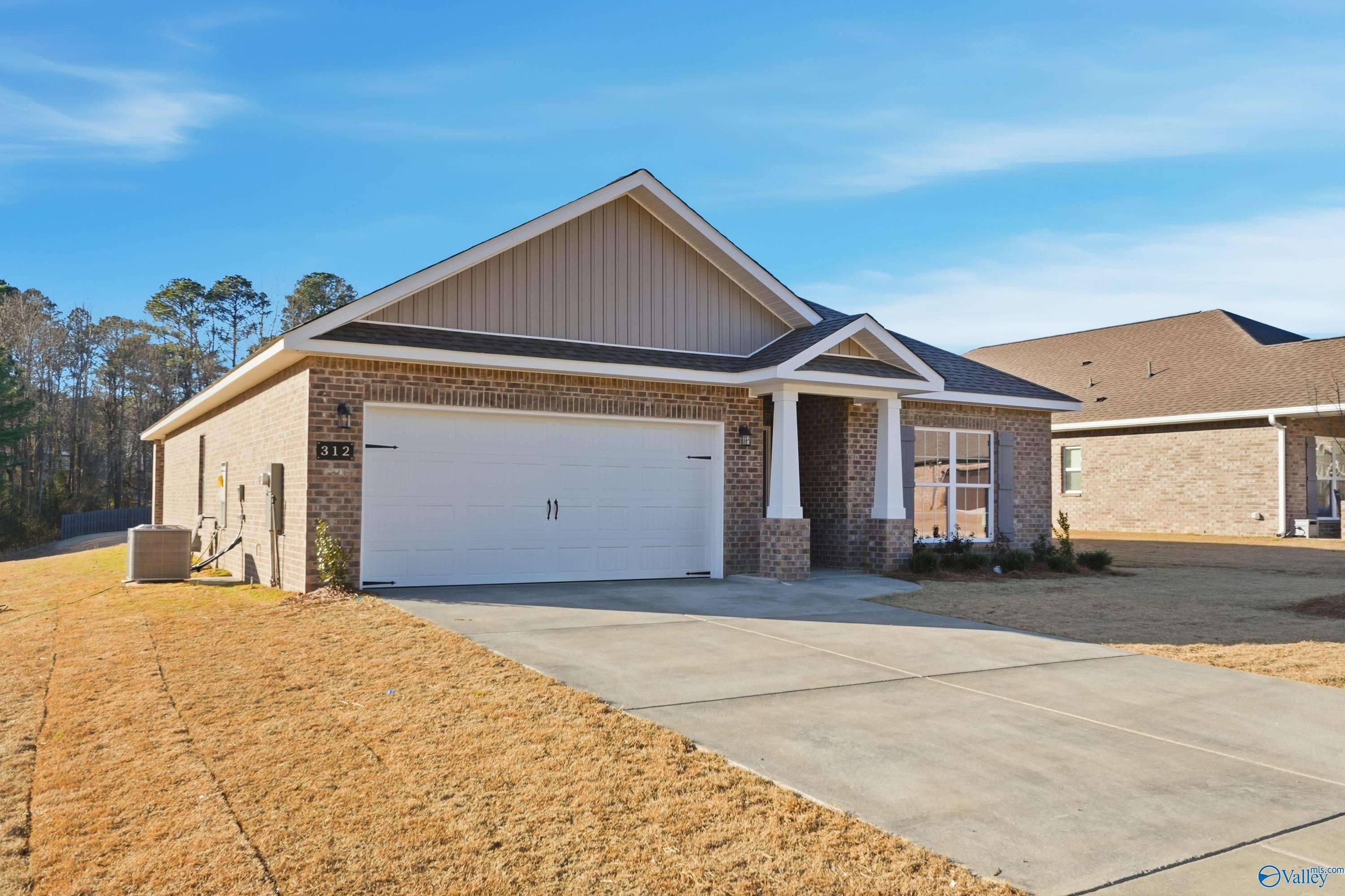 Modern beige brick single-story home with 2-car garage, front porch columns, and pine backdrop in The Highlands, Arab, Alabama