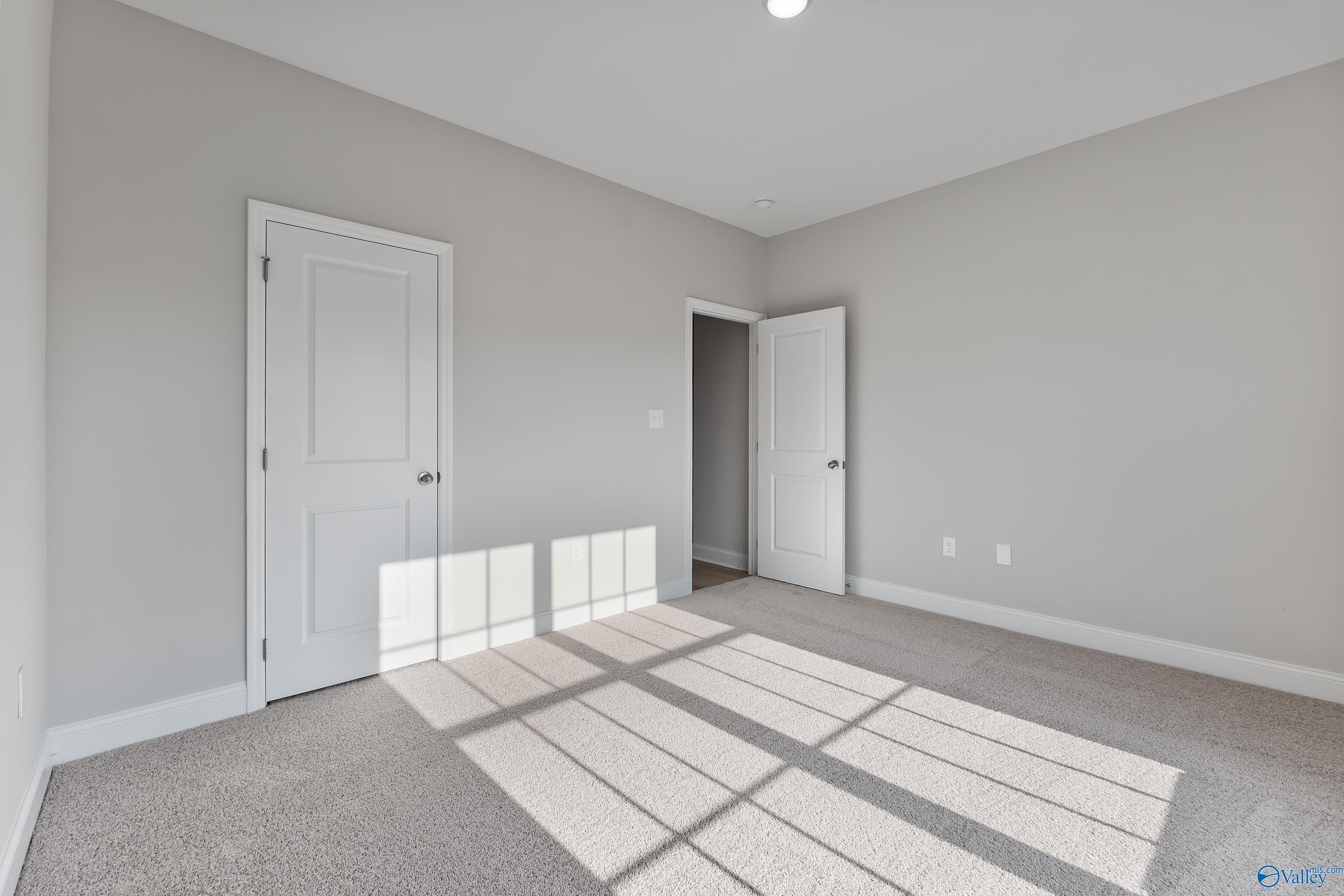 Empty bedroom with gray walls, carpet floor, white doors, and natural sunlight in Davidson Homes The Daphne C, Huntsville, Alabama