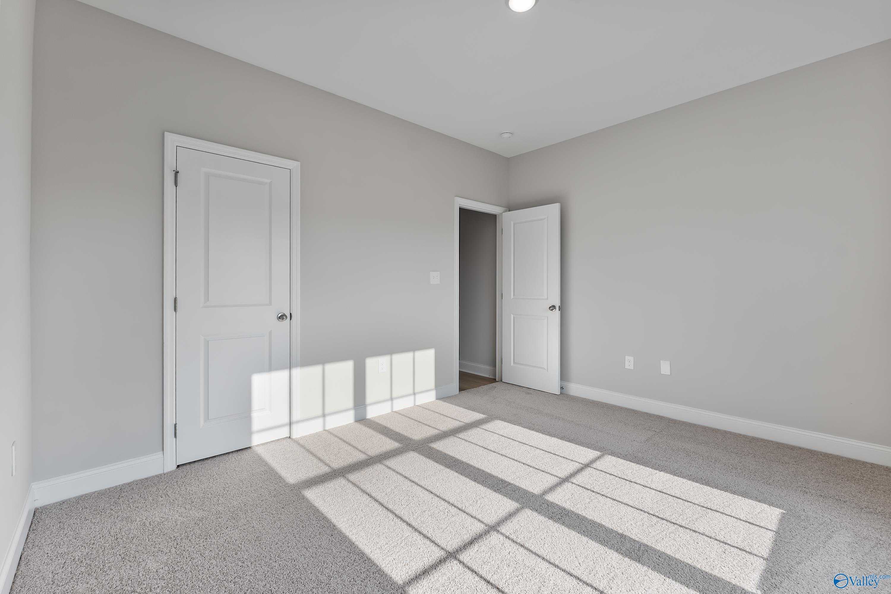 Empty bedroom with gray walls, white doors, and sunlit carpet in The Daphne C 4-bedroom home, Huntsville, Alabama