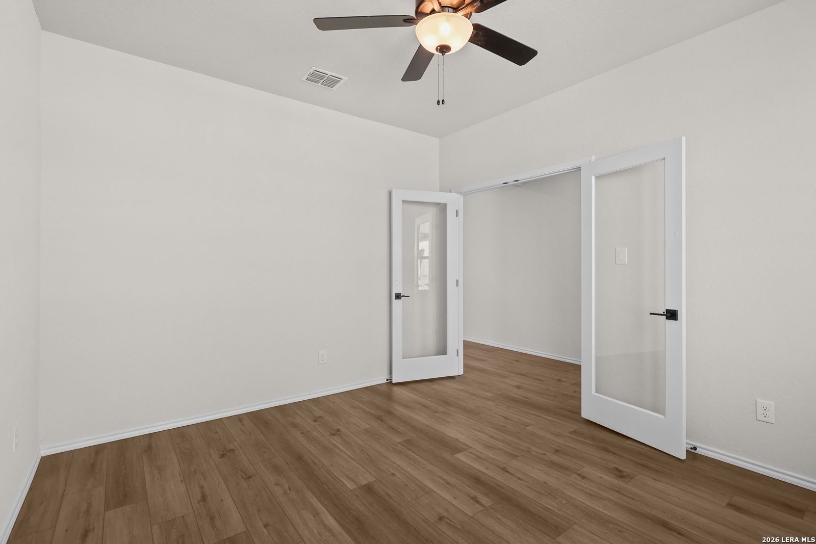 Flexible bedroom with wood-look flooring, ceiling fan, and glass panel doors in Davidson Homes The Glenwood E, San Antonio, TX