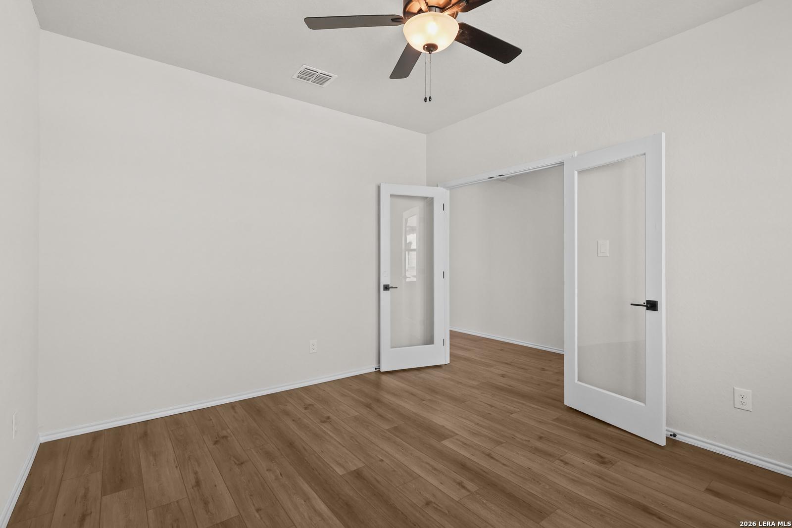 Flexible bedroom with wood-look flooring, ceiling fan, and glass panel doors in Davidson Homes The Glenwood E, San Antonio, TX