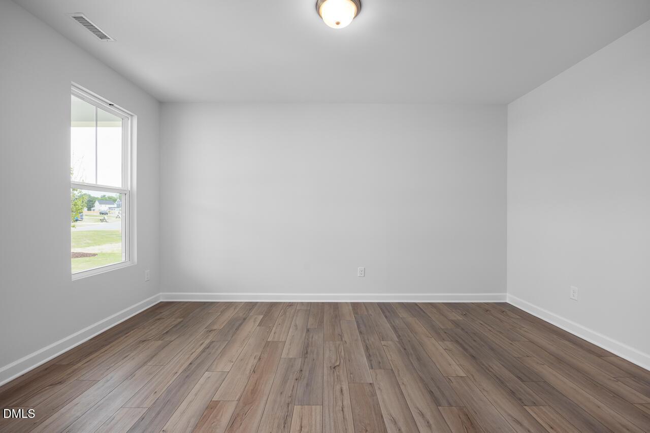 Empty bedroom featuring hardwood floors, white walls, and large window in The Hickory II B by Davidson Homes, Zebulon, NC