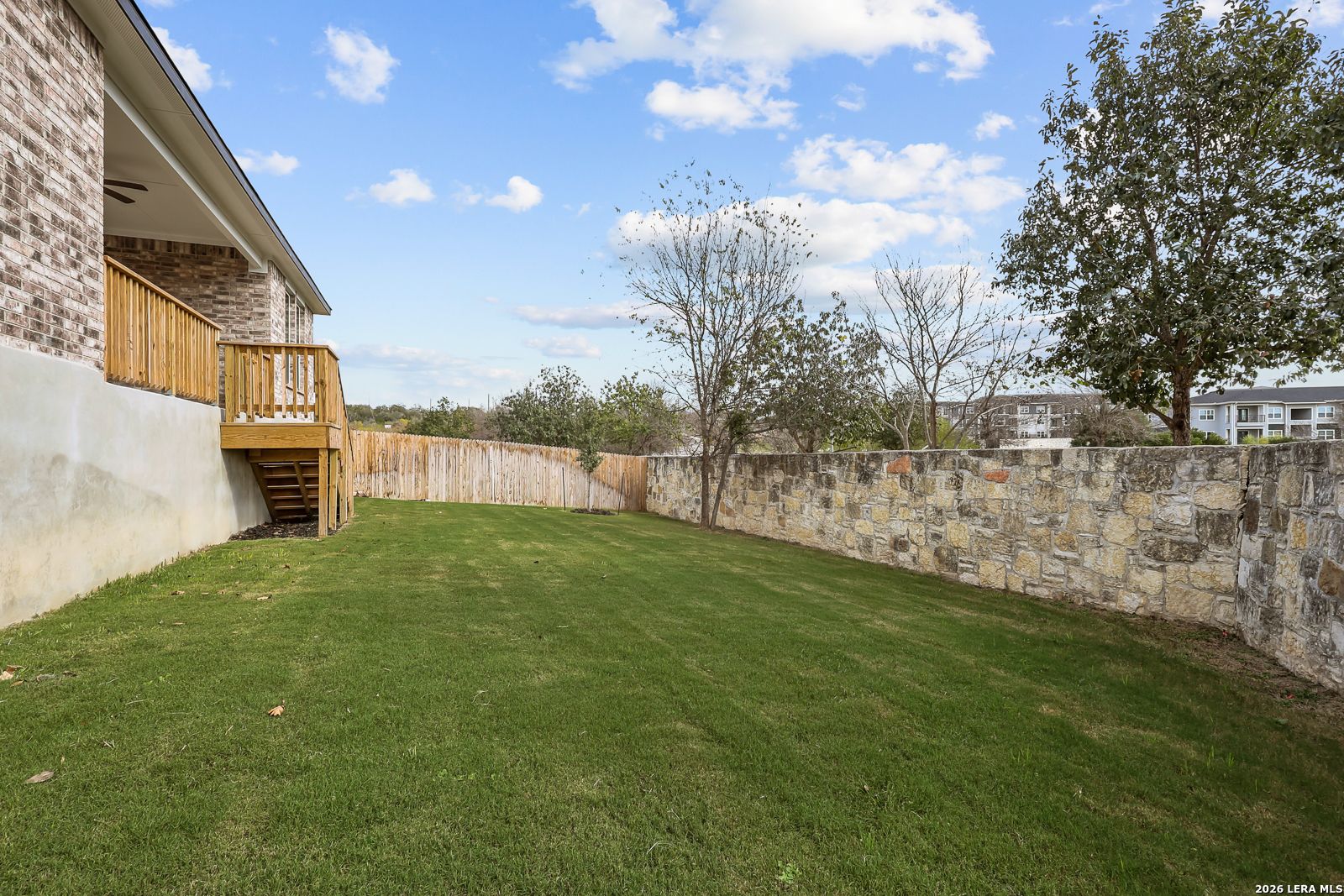 Private backyard with wooden deck and stone wall at The Lanier H floor plan home in Ladera, San Antonio, Texas.