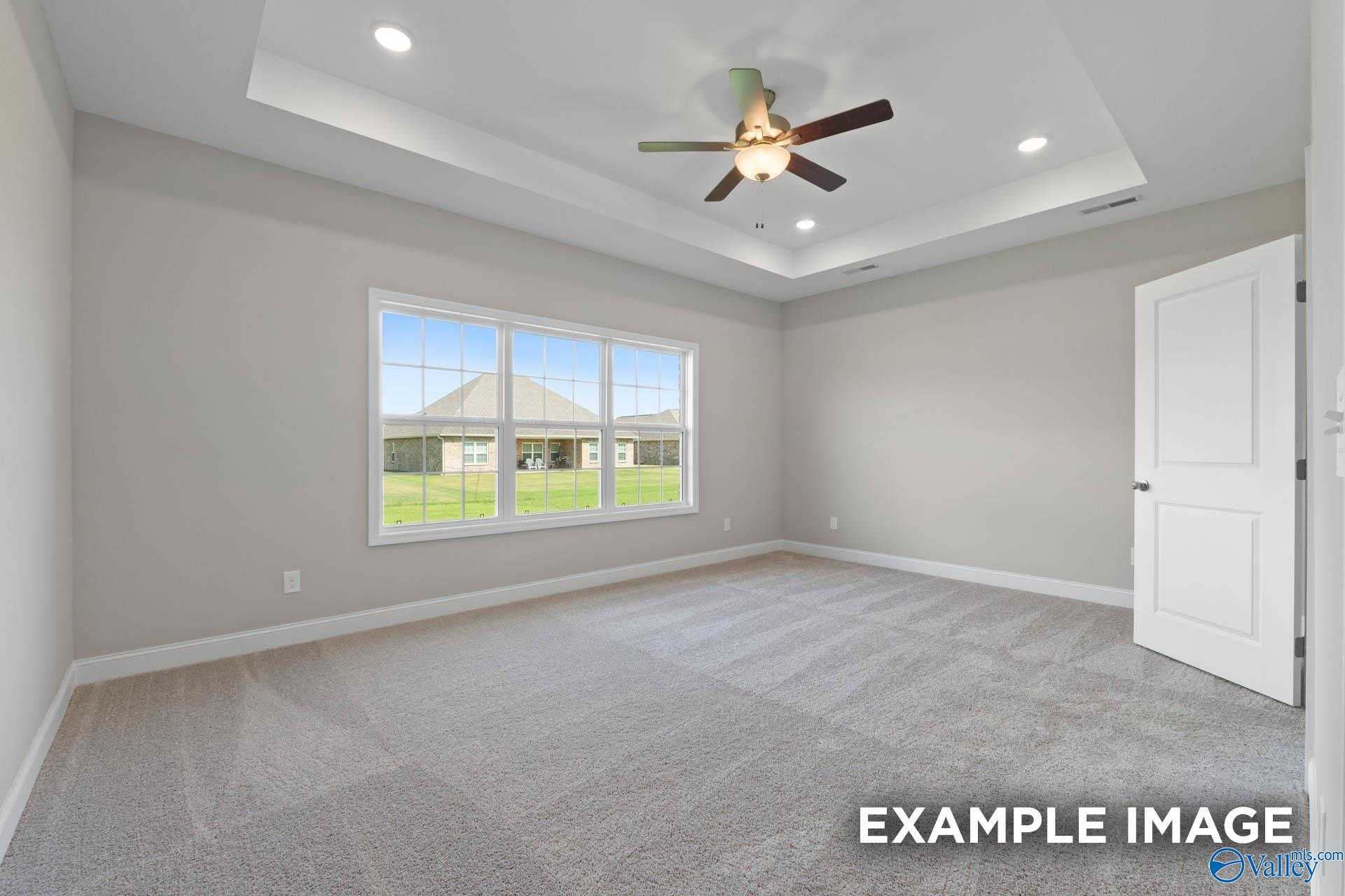 Bright bedroom with tray ceiling, ceiling fan, and large window overlooking lush backyard in Davidson Homes The Montgomery B, Hartselle