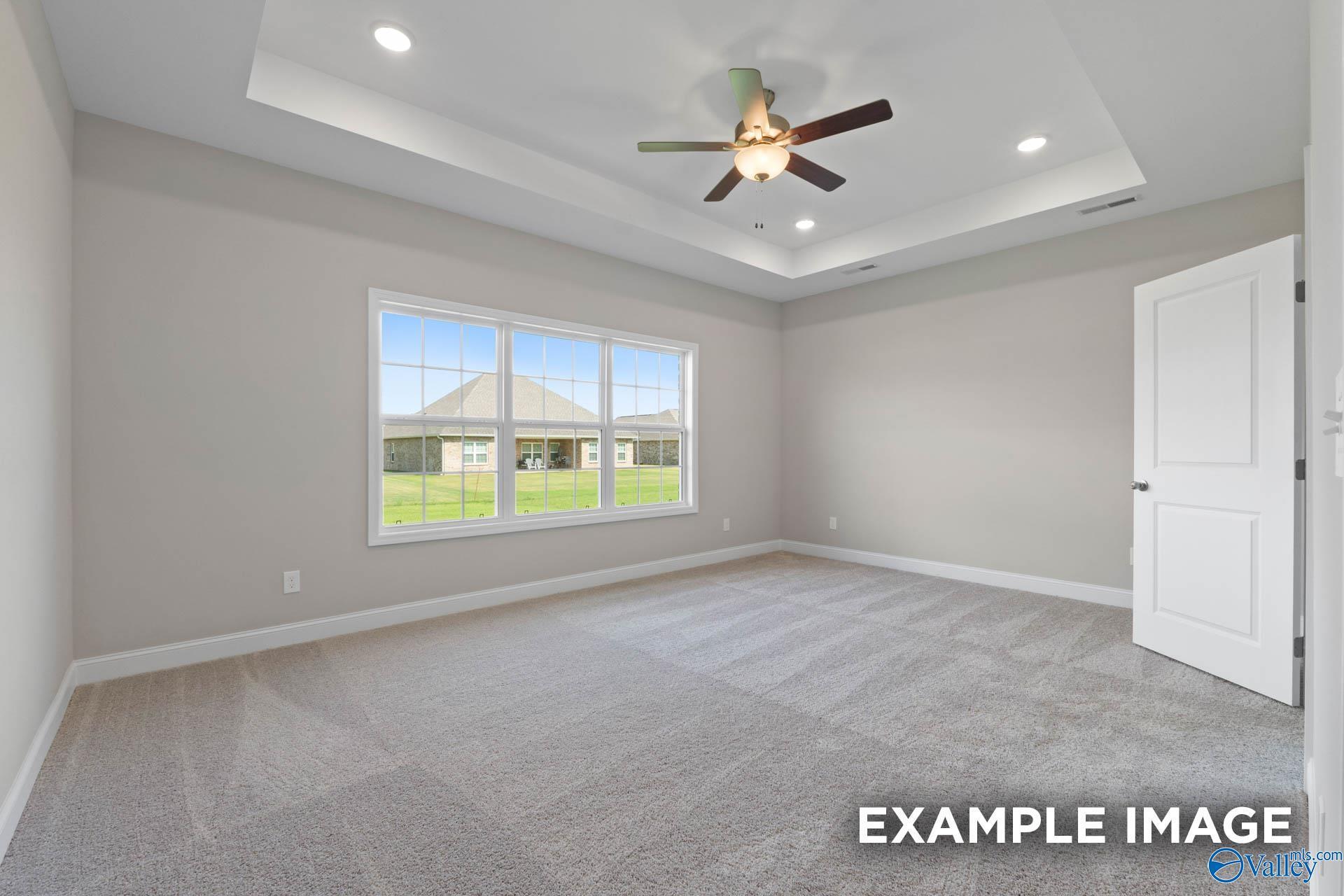 Bright master bedroom with ceiling fan, tray ceiling, and large windows overlooking lawn in Davidson Homes The Montgomery B, Hartselle, Alabama