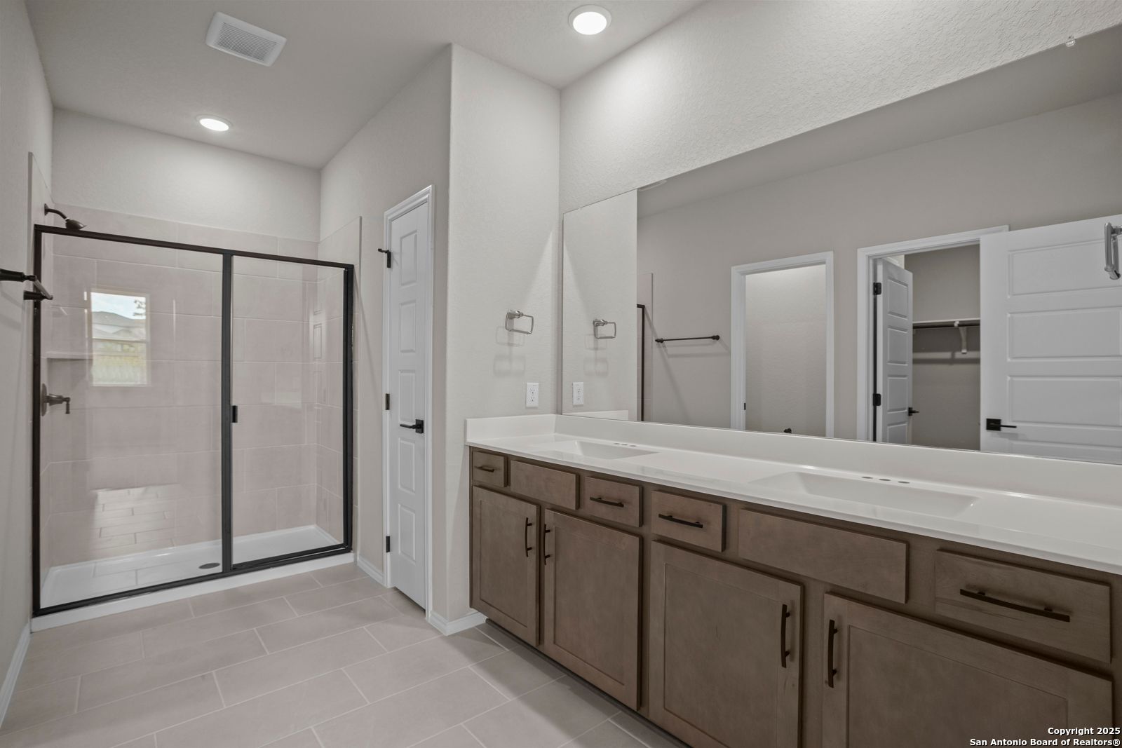 Modern master bathroom with frameless glass shower, double wood vanity, and walk-in closet in Davidson Homes The Douglas F, San Antonio