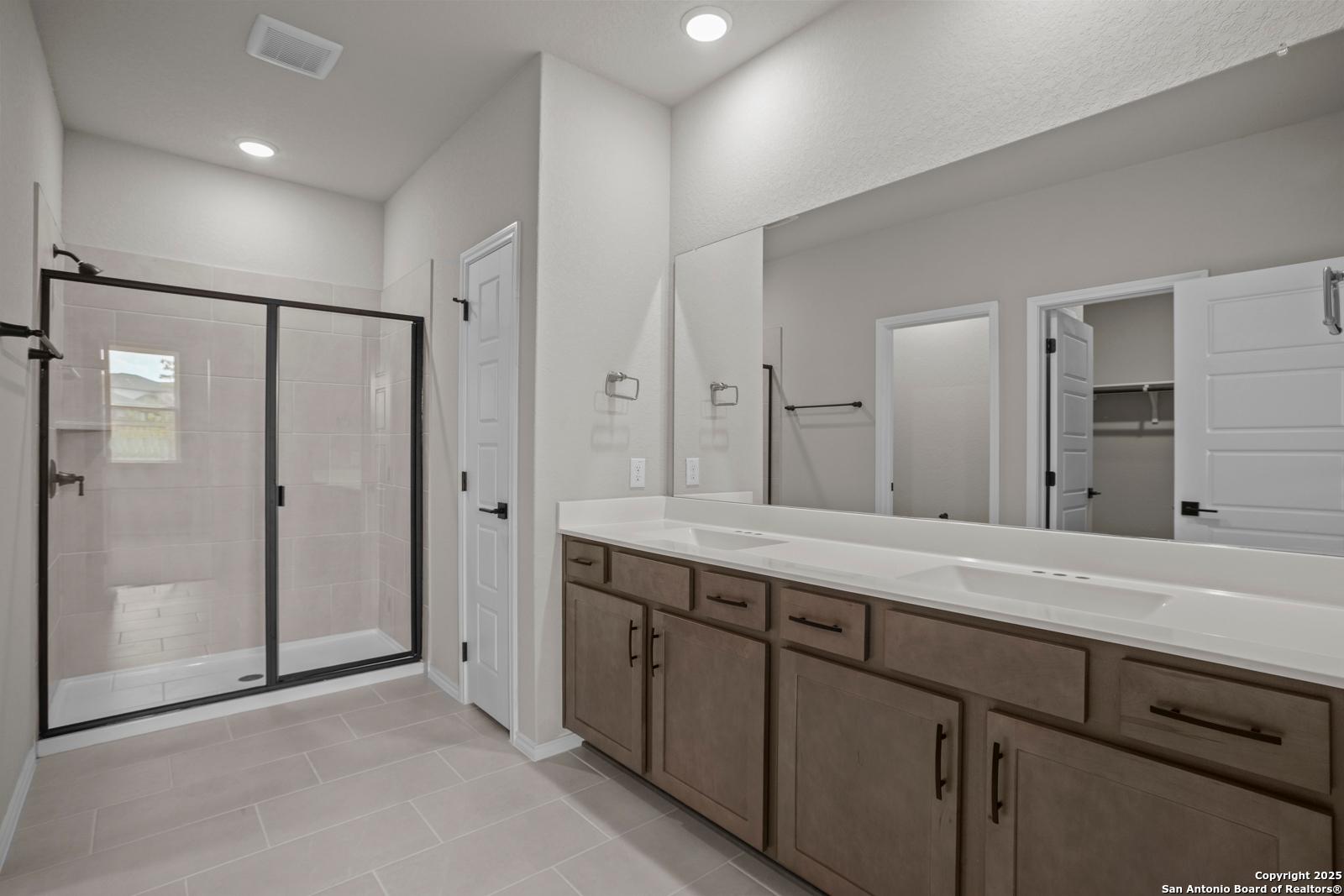 Modern master bathroom with frameless glass shower, double wood vanity, and walk-in closet in Davidson Homes The Douglas F, San Antonio