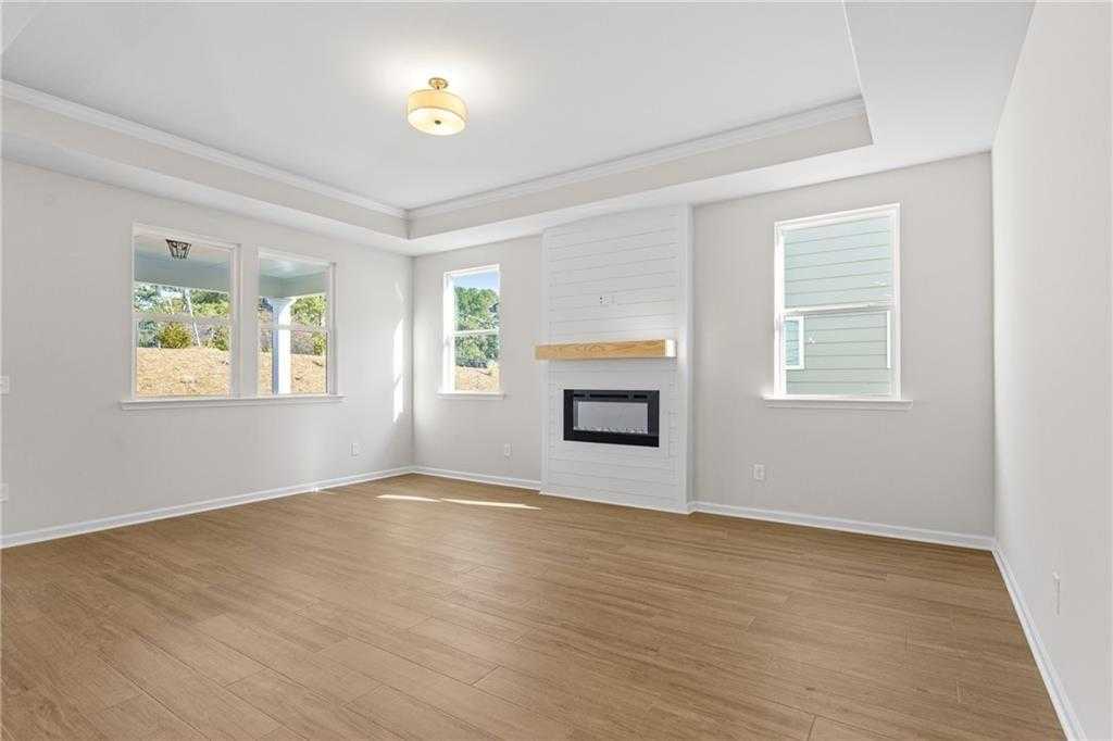 Bright living room with gas fireplace, white shiplap surround, large windows, hardwood floors in Davidson Homes The Edison A, Loganville, GA