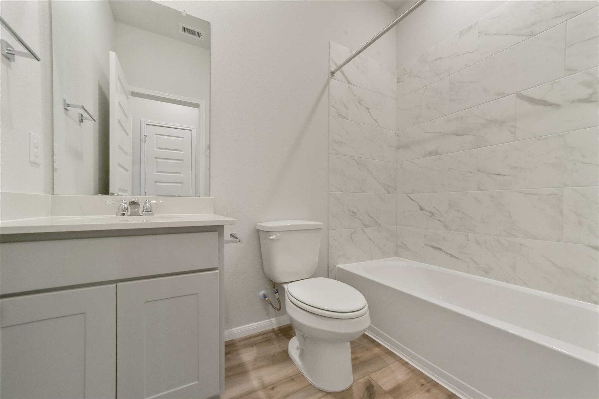Elegant bathroom with white subway tiles, soaking tub, modern vanity, and toilet in Davidson Homes San Marcos E, Beasley TX
