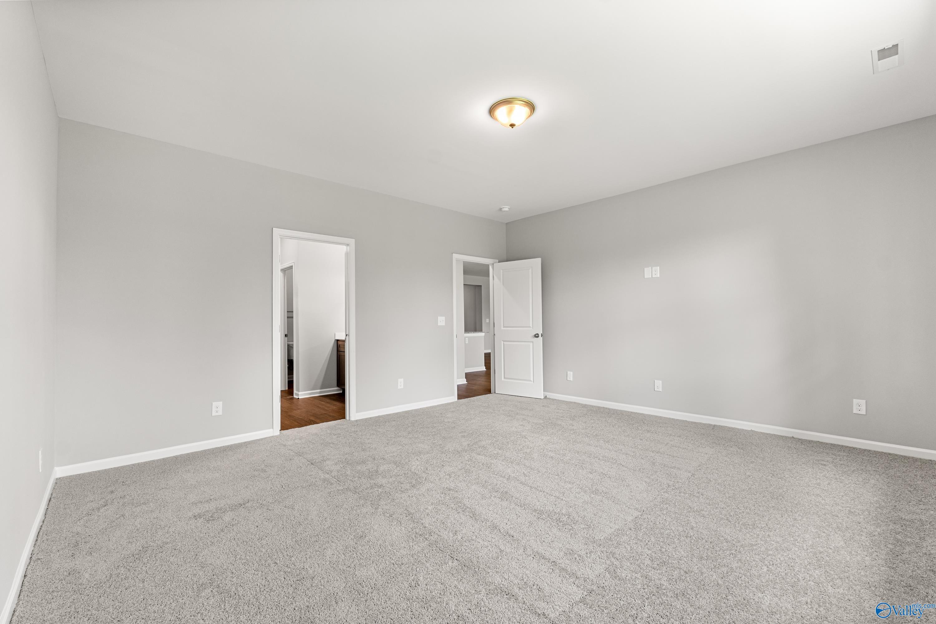 Spacious secondary bedroom with light gray walls, plush carpet, and adjacent bathroom doors in Davidson Homes The Sanctuary, Huntsville, Alabama