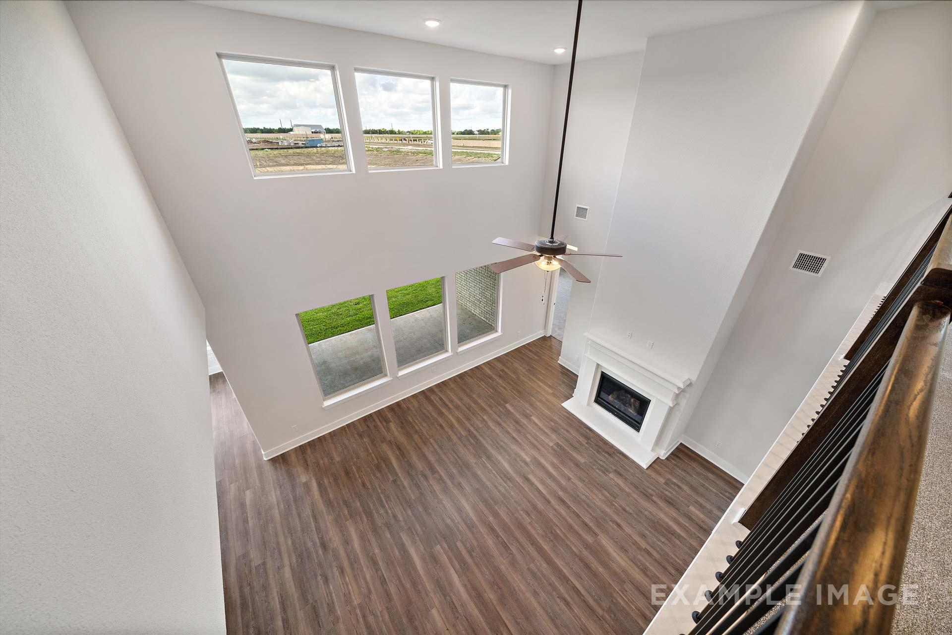 Spacious two-story great room in The Victoria A home design featuring high ceilings, large windows, ceiling fan, gas fireplace, and hardwood floors