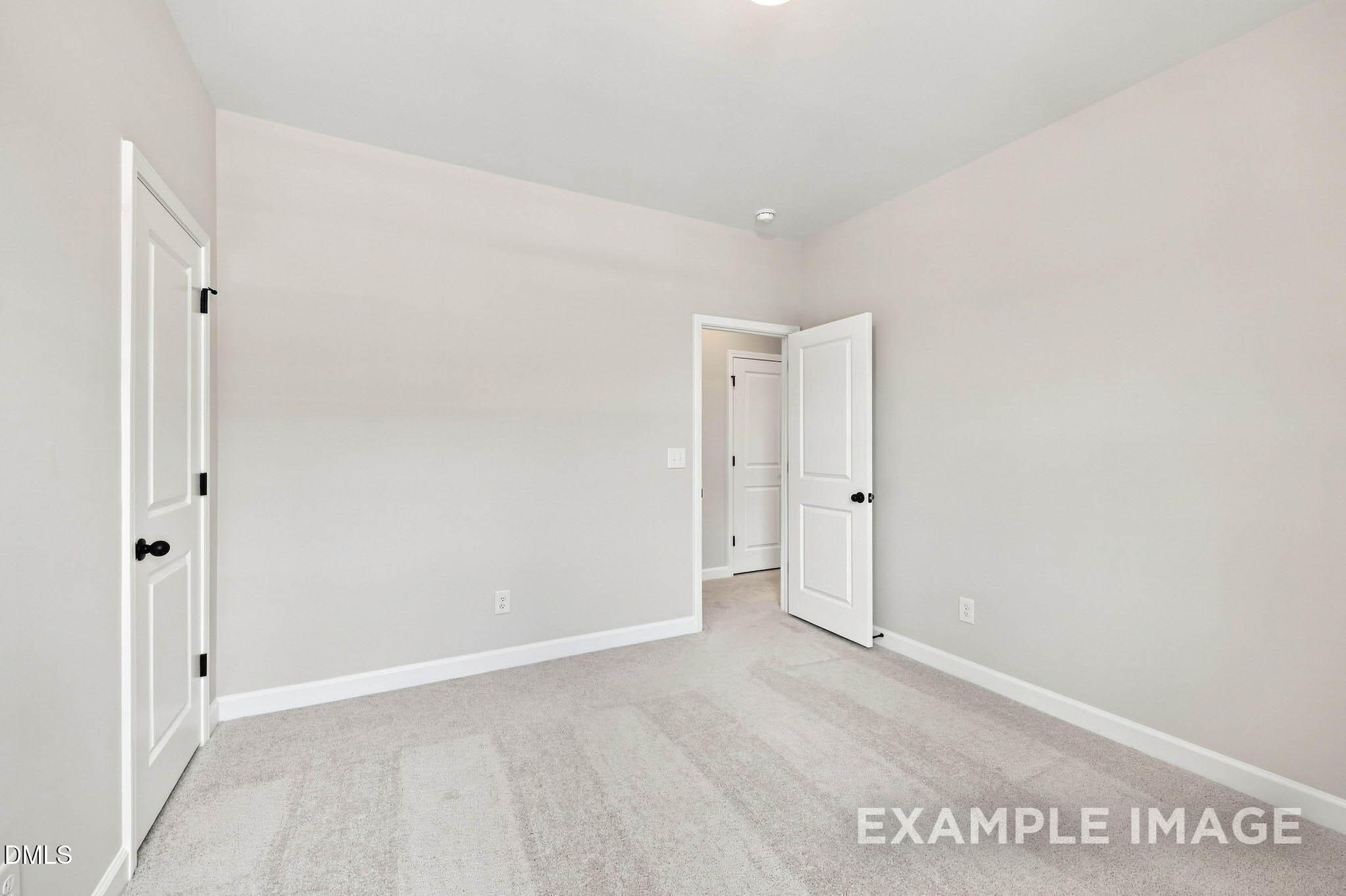 Bright empty bedroom with neutral carpet, white doors, and black hardware in Davidson Homes The Harris A plan, Knightdale NC