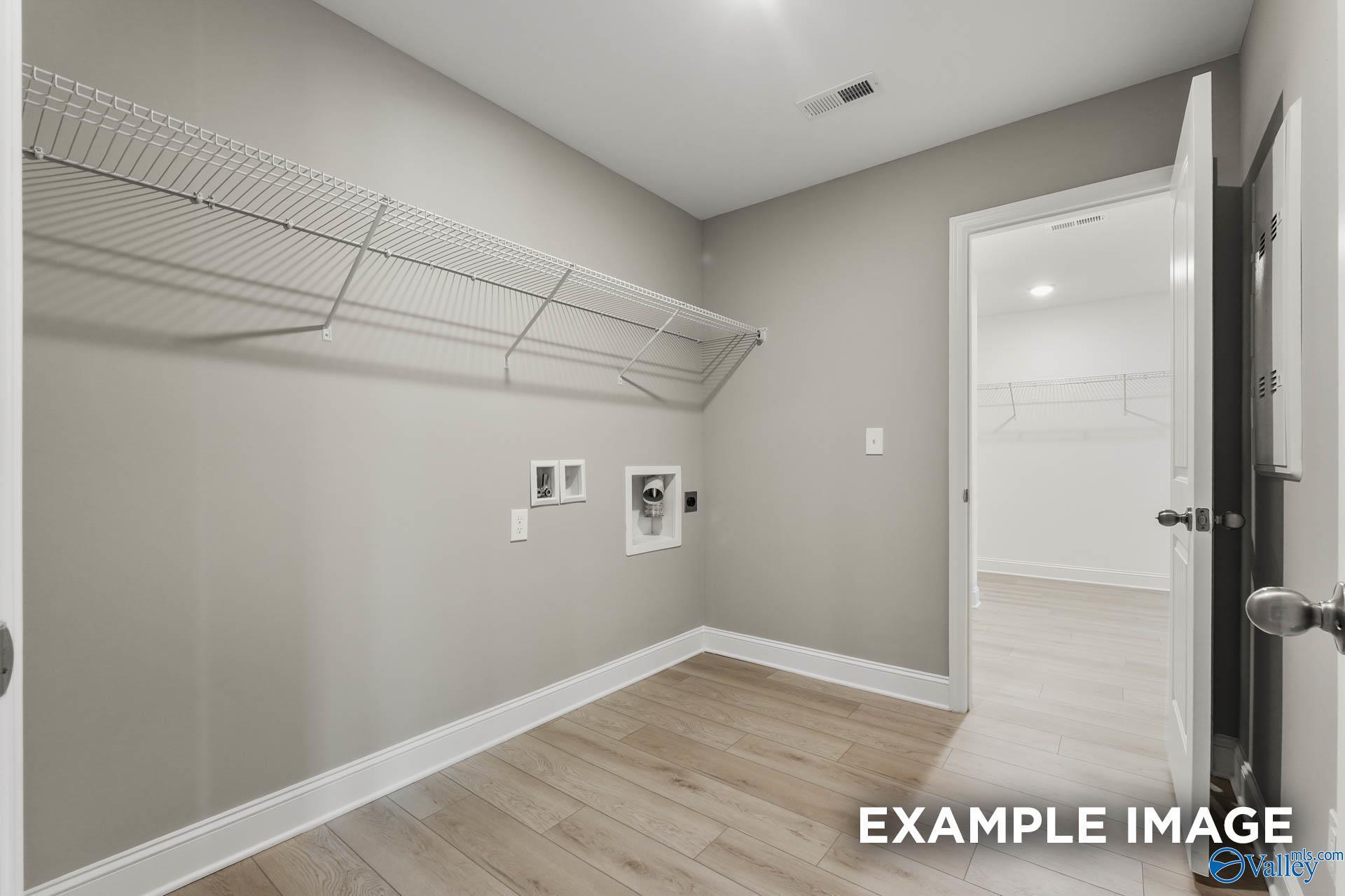 Functional laundry room with gray walls, wire shelving, washer-dryer hookups in The Everett B, Davidson Homes, Wood Trail Toney AL