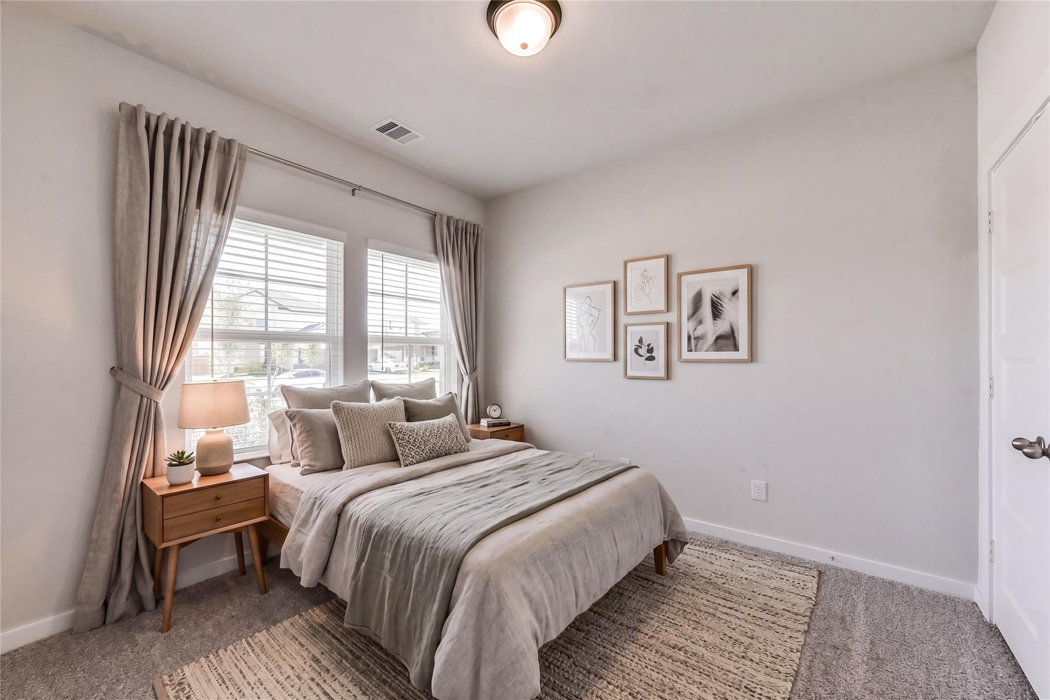Serene neutral bedroom with queen bed, gray linens, wooden nightstand, potted plant, window curtains in Davidson Homes Costa C, Dayton TX