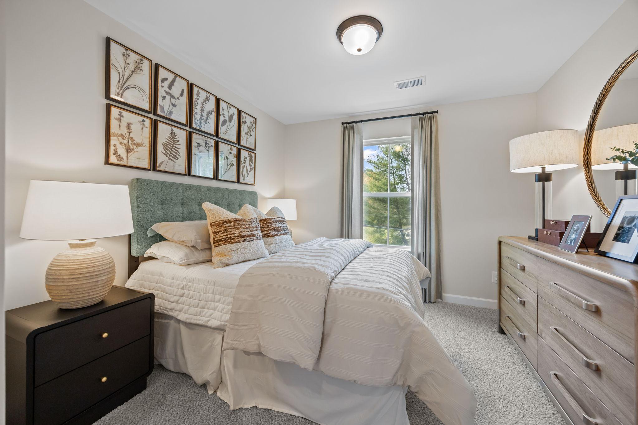 Cozy bedroom in Camden Park Knightdale NC with teal upholstered headboard, white bedding, botanical wall art, and tree-view window