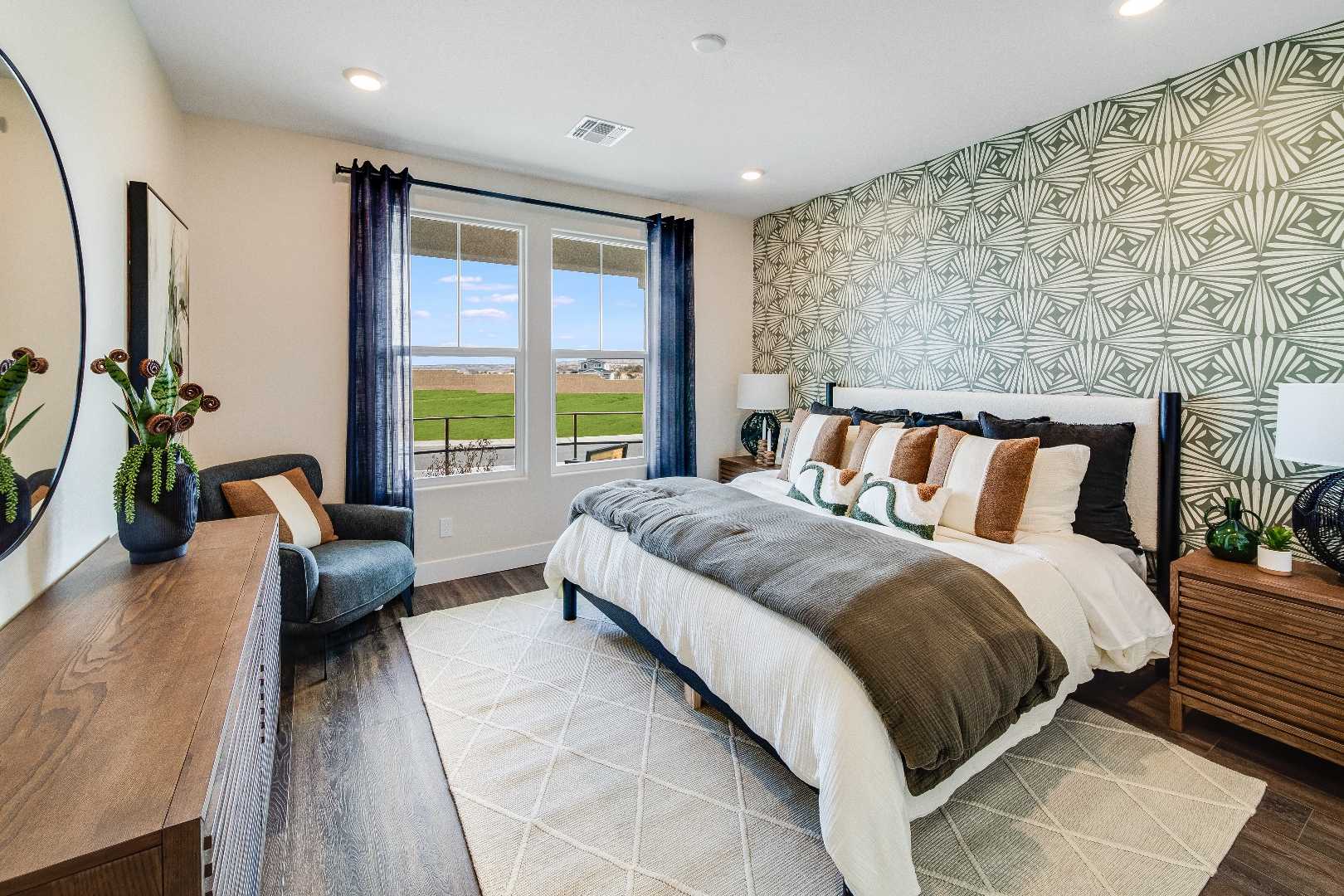The Boulder II master bedroom featuring king bed with gray bedding, green geometric wallpaper, wooden furniture, and scenic window view