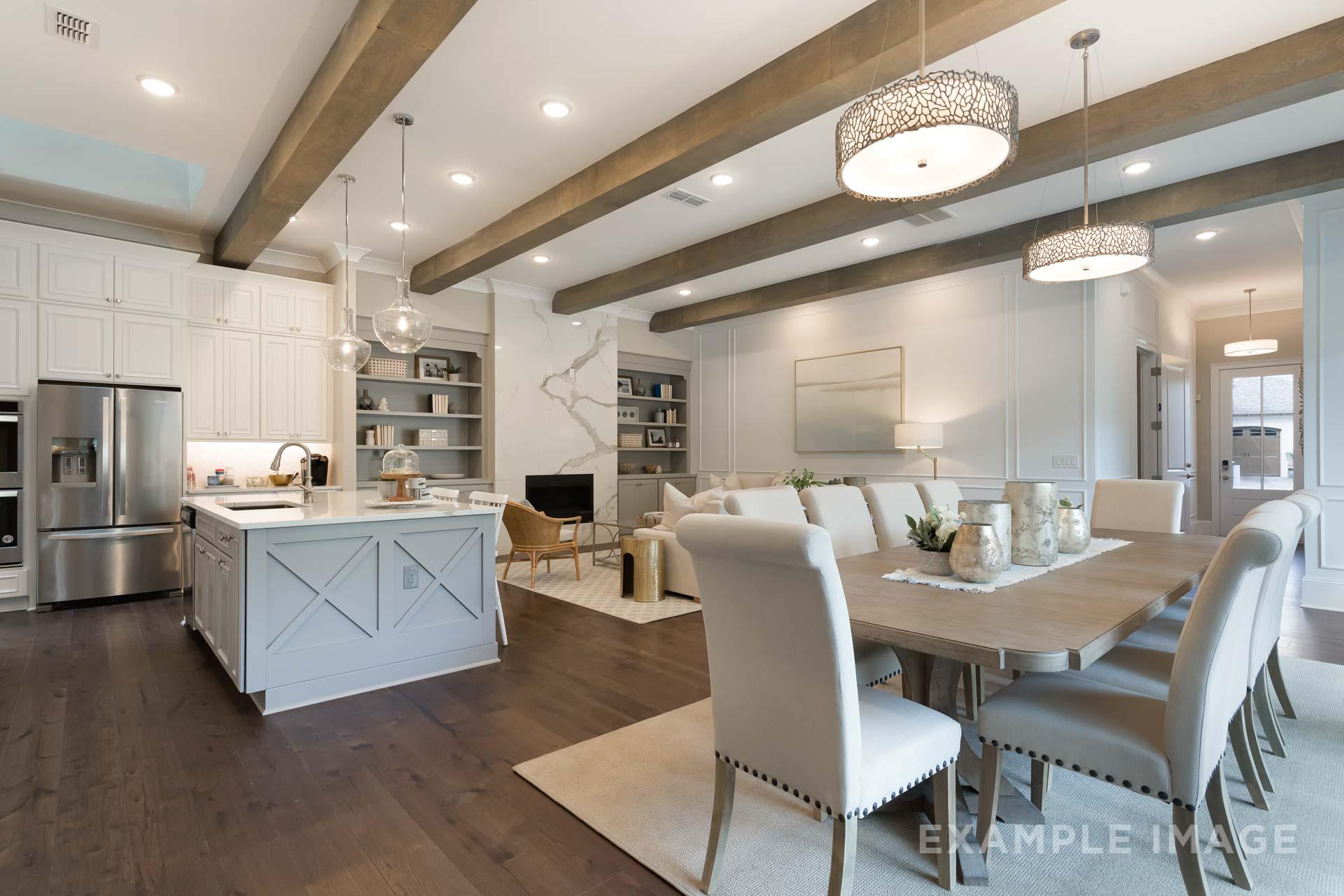 Spacious open-concept kitchen and dining in The Seaside home featuring white shaker cabinets, large gray island, exposed wood beams, and pendant lights
