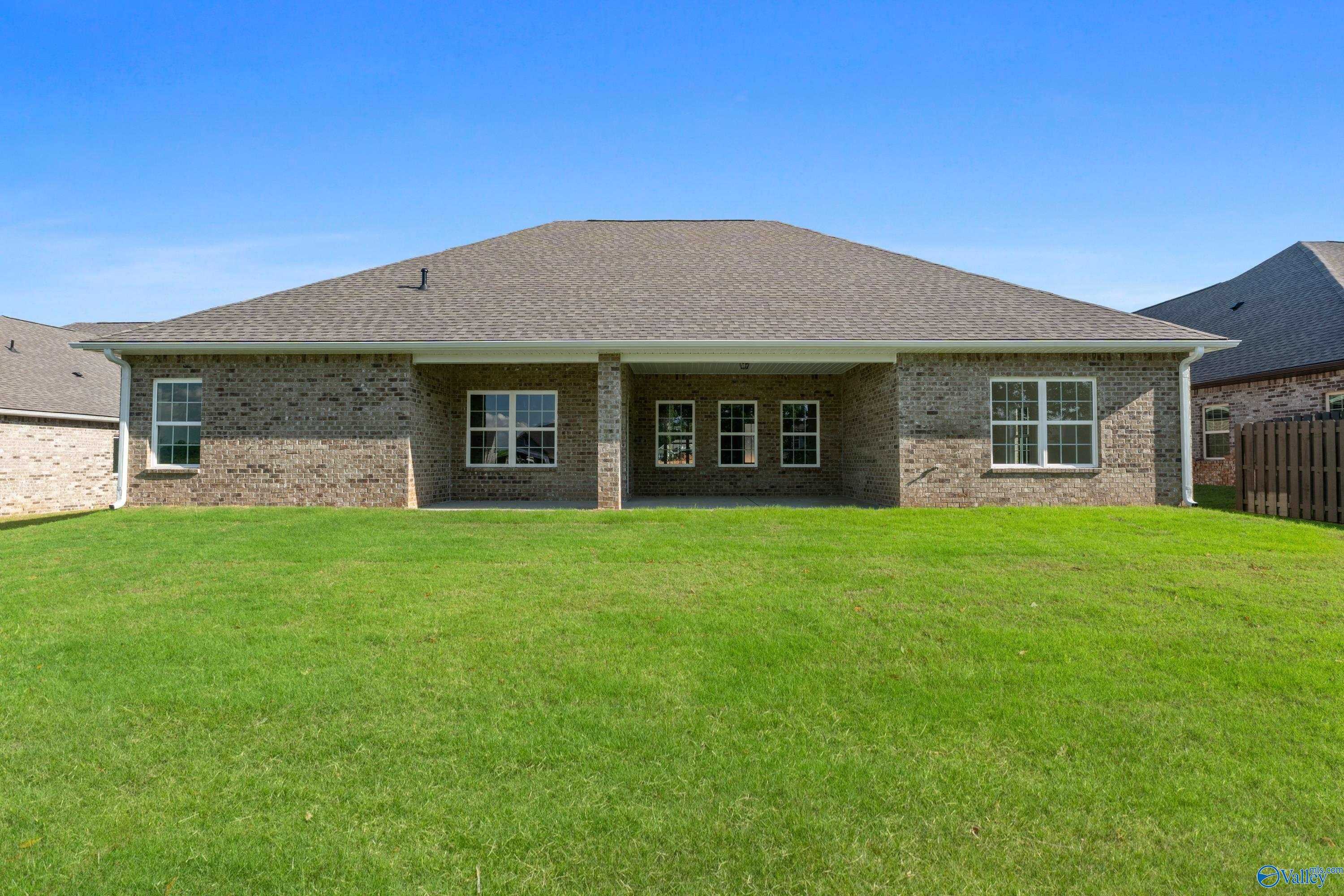 Rear view of The Oxford 1-story brick home by Davidson Homes, covered patio, large windows, lush green lawn in Creekside, Harvest, AL