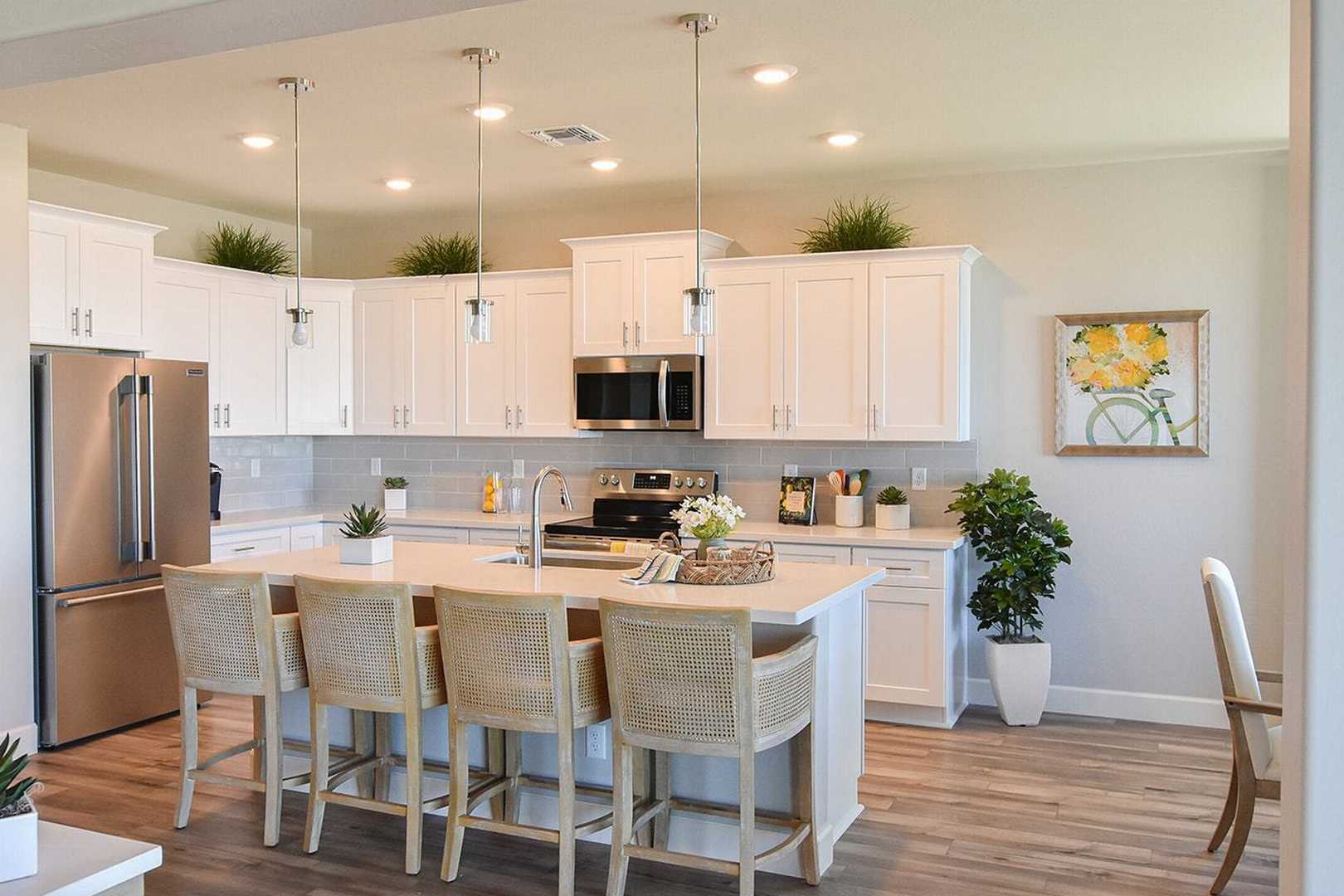 Spacious white kitchen in The Summit B featuring large island with wicker stools, stainless steel appliances, pendant lights, and potted plants