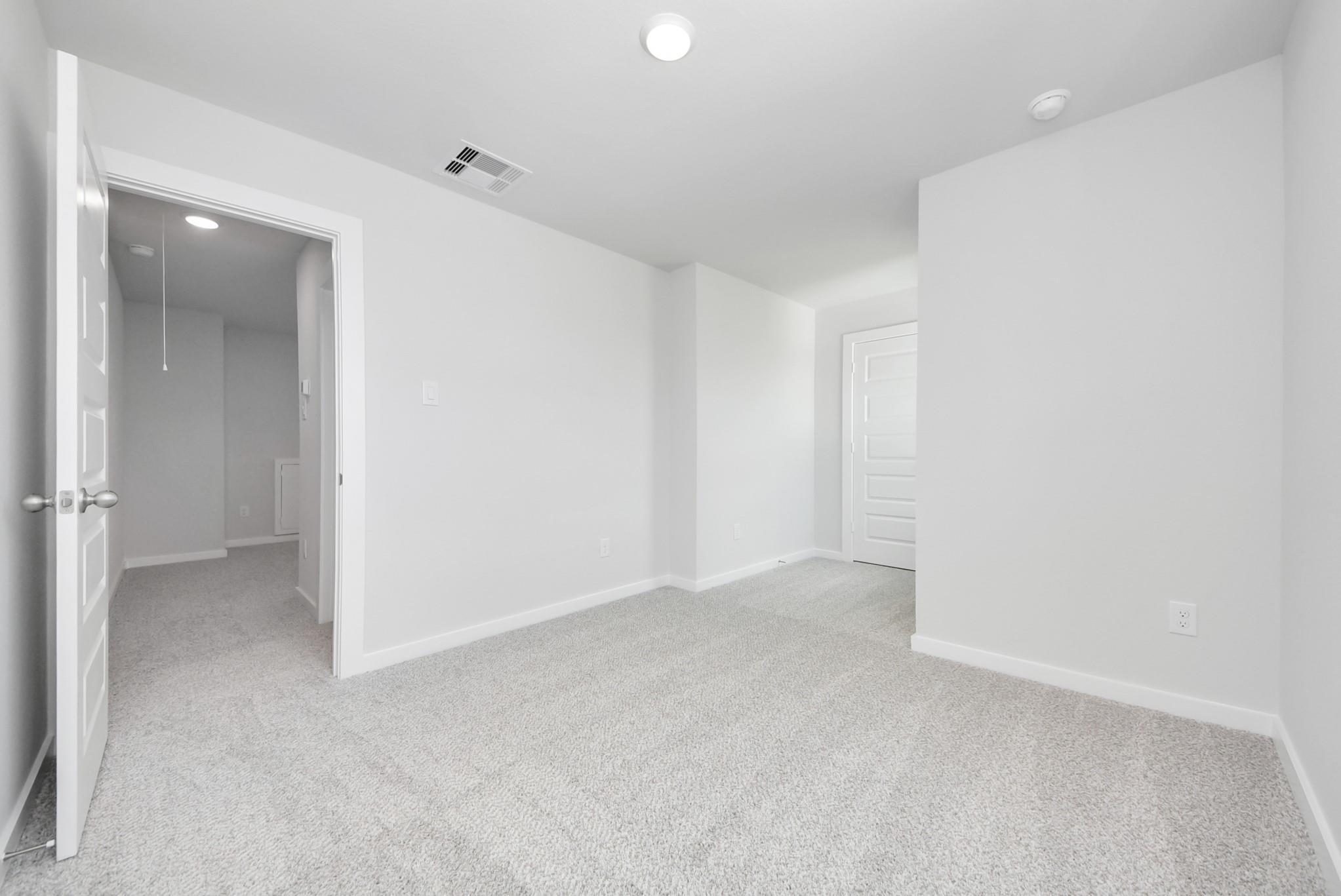 Bright, neutral-toned bedroom with plush carpeting in The Blanco F floor plan at Spring Branch Crossing, Conroe, Texas.
