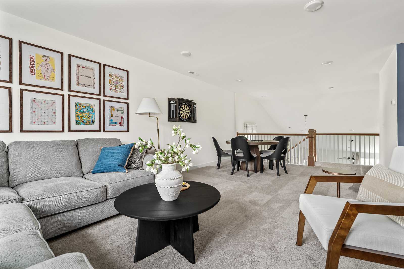 Spacious loft bonus room at Woods Crossing in Gallatin TN with gray sectional sofa, black coffee table, dining area, and colorful framed art