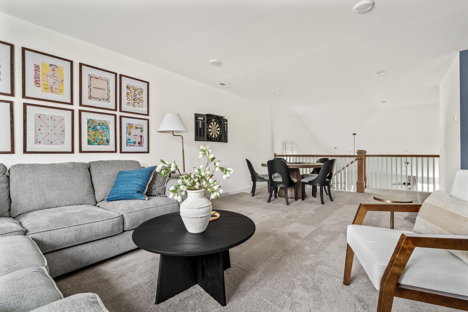 Spacious loft bonus room at Woods Crossing in Gallatin TN with gray sectional sofa, black coffee table, dining area, and colorful framed art