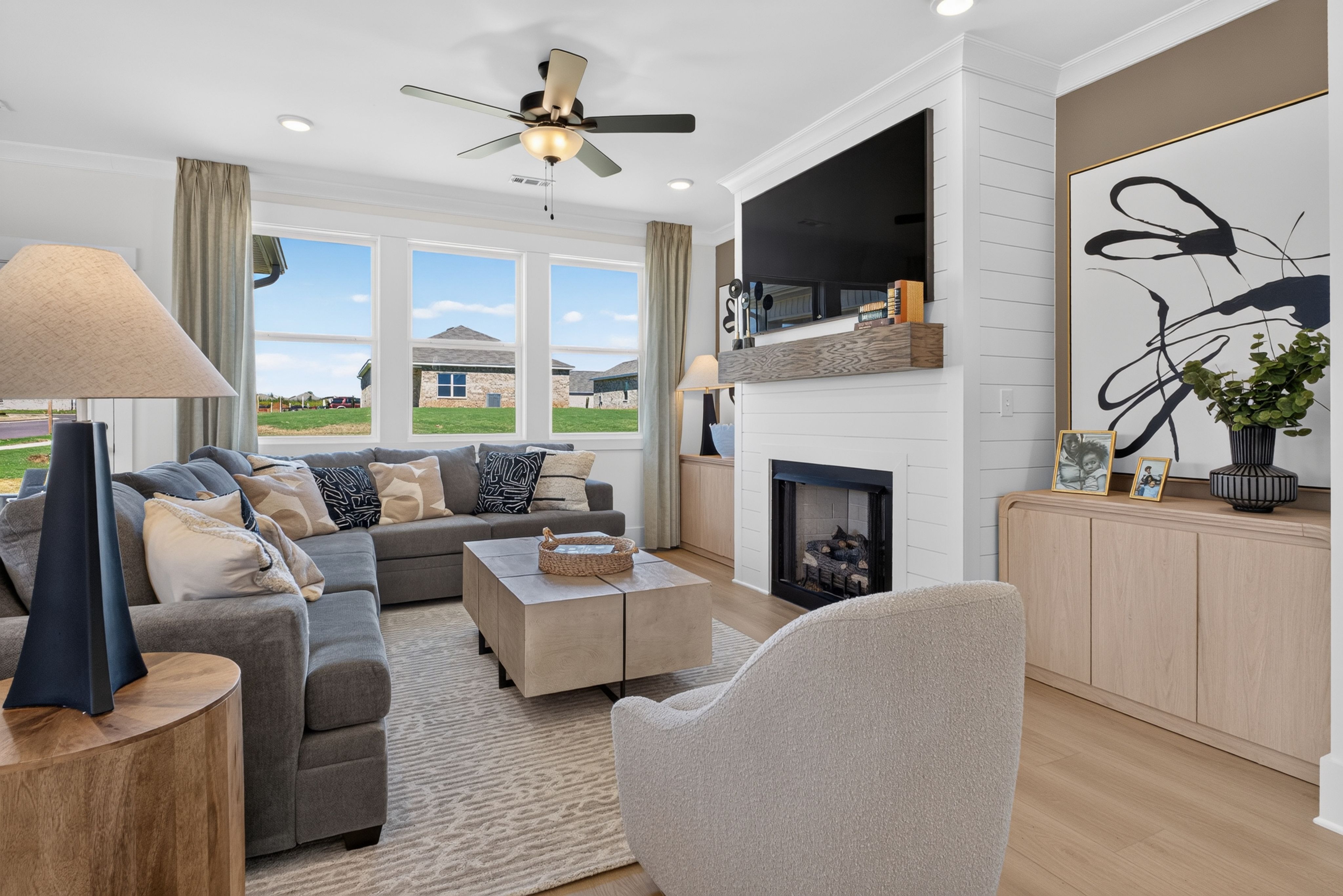 Bright great room at Evergreen Mill in Madison, Alabama by Davidson Homes with gray sectional, fireplace, and large windows