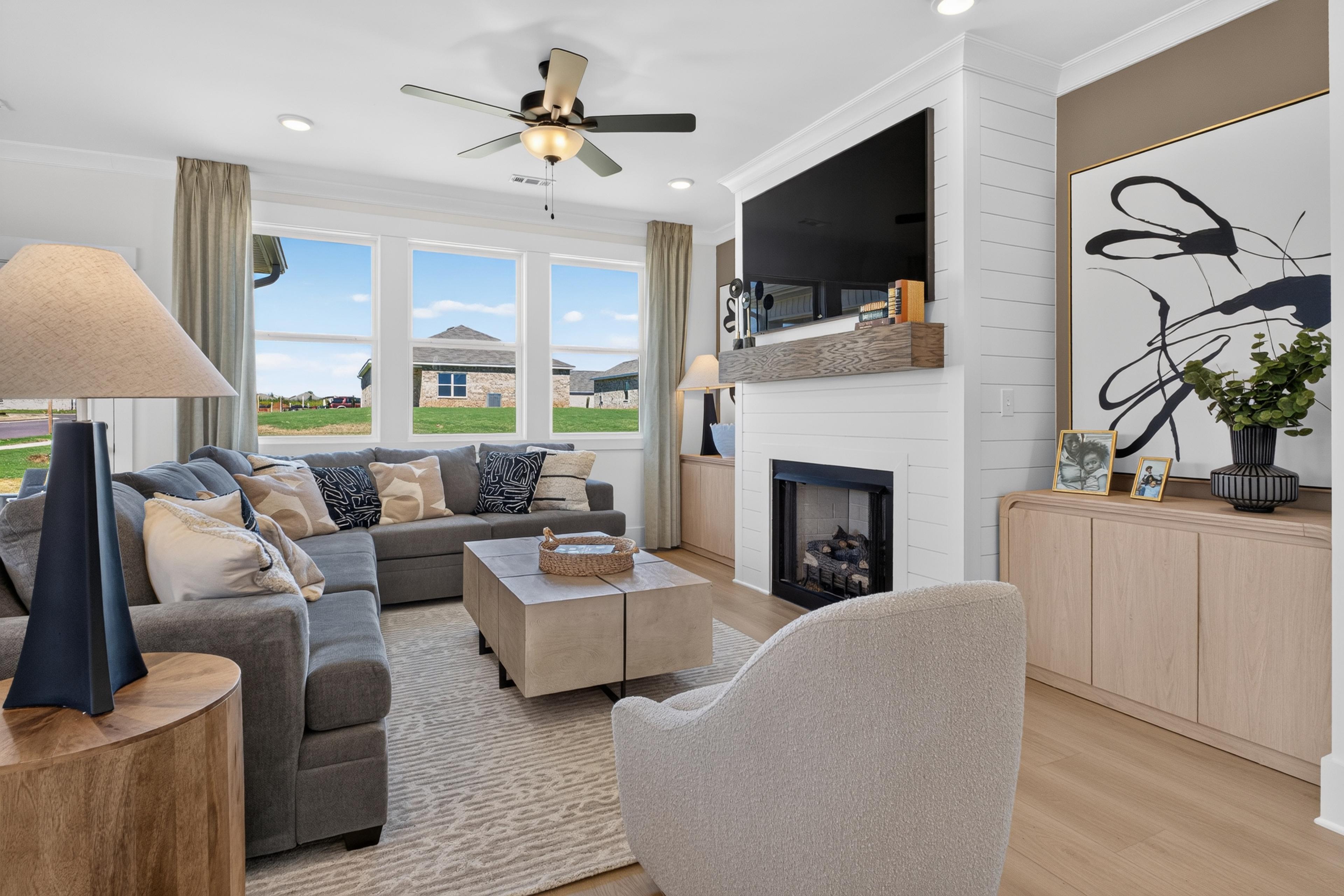 Bright great room at Evergreen Mill in Madison, Alabama by Davidson Homes with gray sectional, fireplace, and large windows