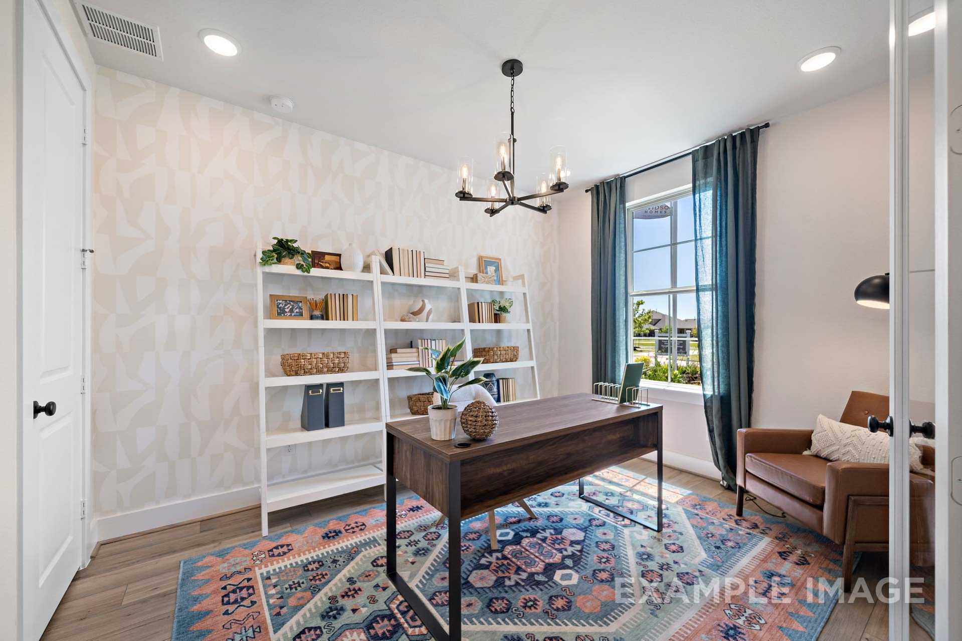 Spacious home office in The Edward B featuring white built-in bookshelves, wooden desk, potted plants, colorful rug, and large window