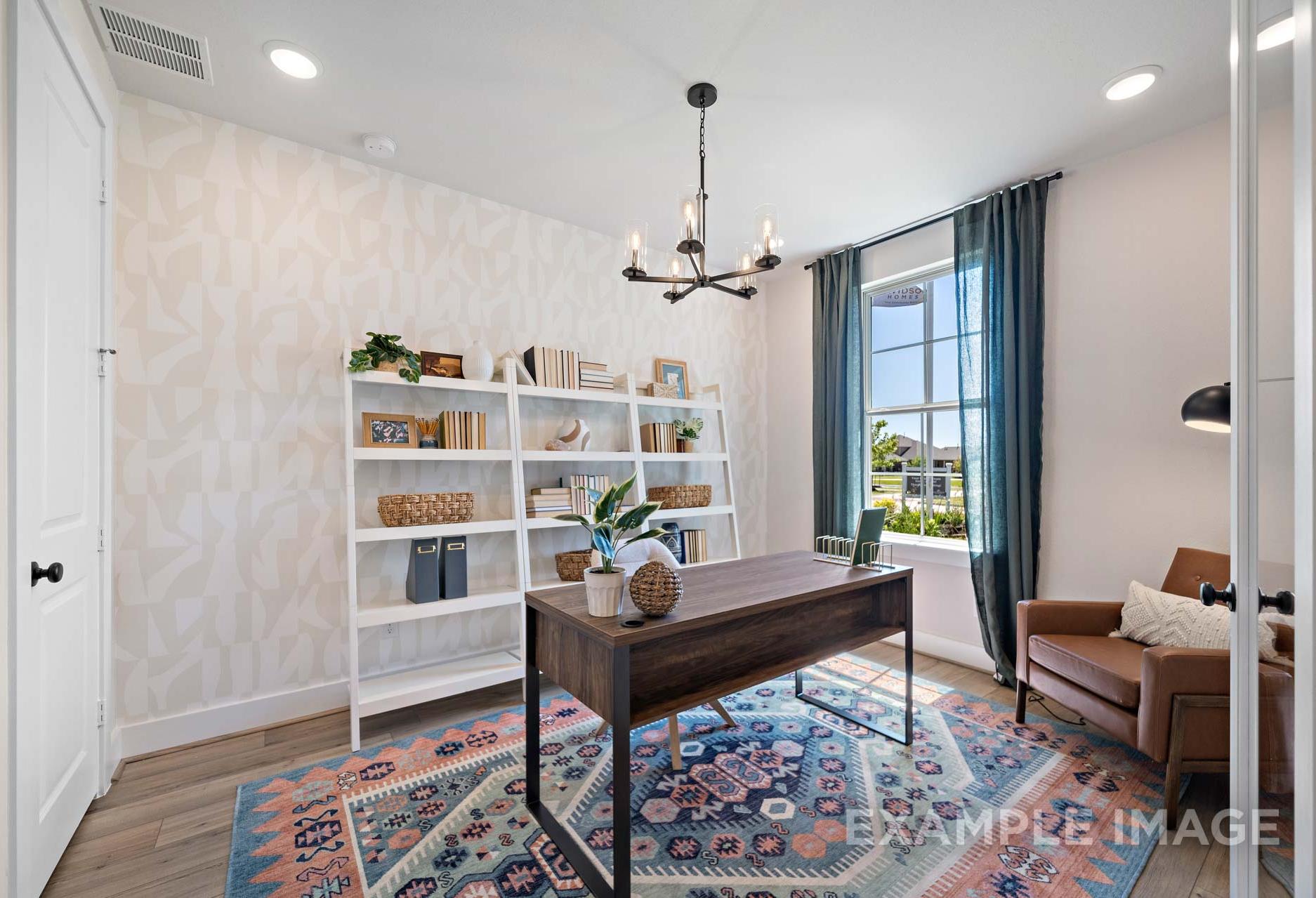 Spacious home office in The Edward A Davidson Homes design featuring wooden desk, white bookshelves, chandelier, and blue rug