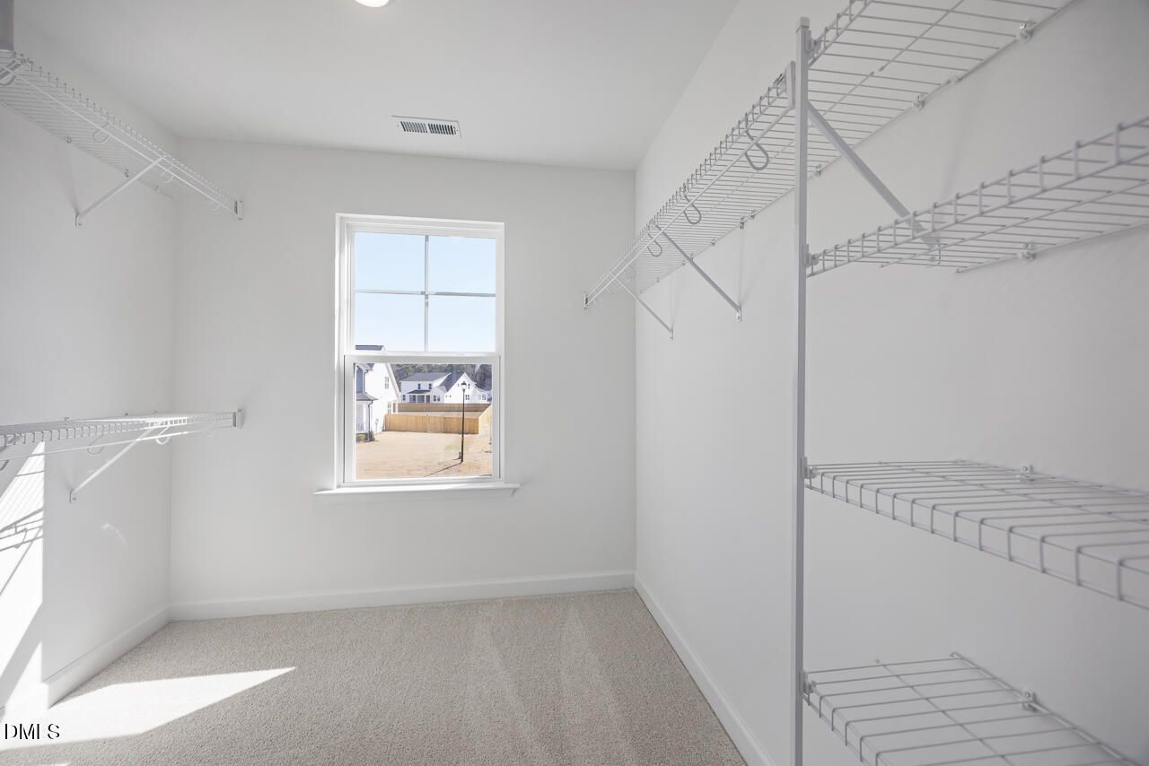 Spacious walk-in closet with wire shelving, hanging rods, and window view in Davidson Homes The Willow G, Angier, NC
