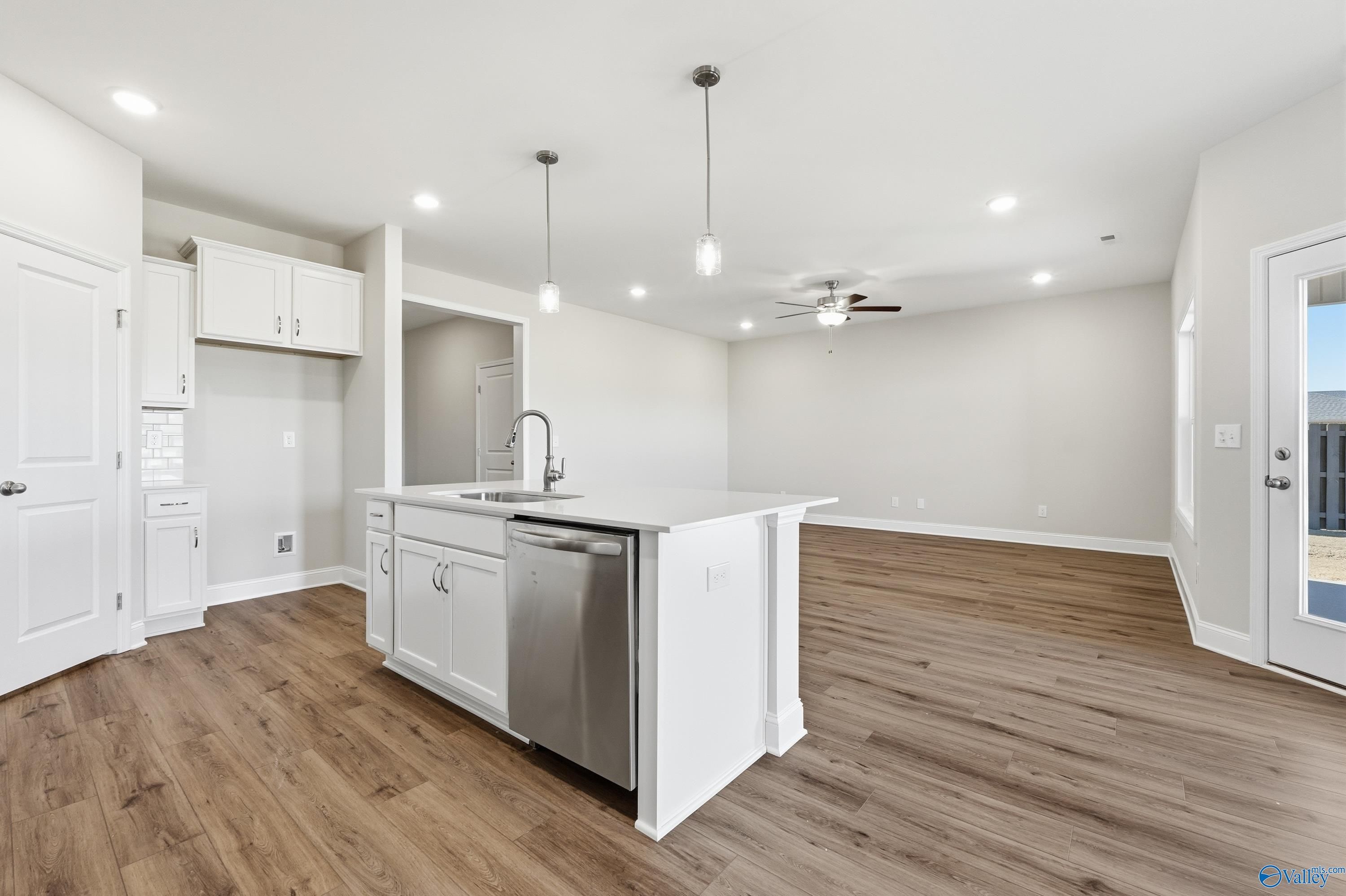 Modern open-concept kitchen with white island, sink, dishwasher, hardwood floors and ceiling fan in The Everett plan, Harvest AL
