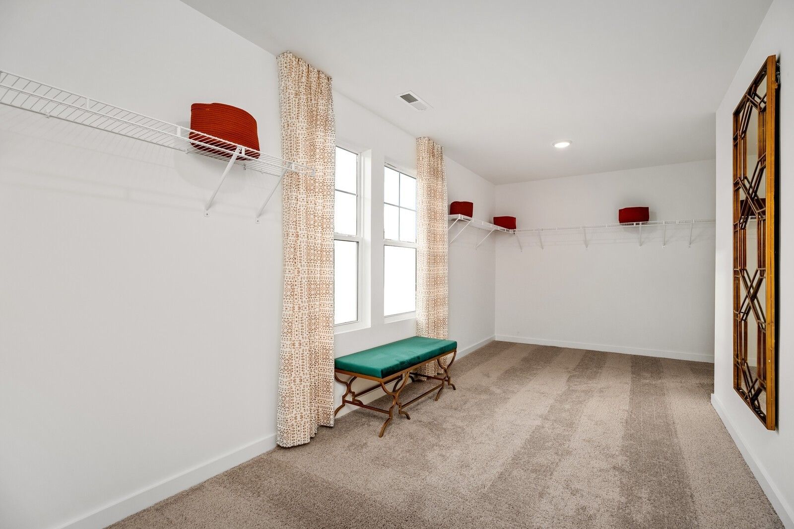 Spacious walk-in closet with wire shelving, red bins, beige curtains, green bench, ornate mirror in Davidson Homes The Gordon C, White House, TN
