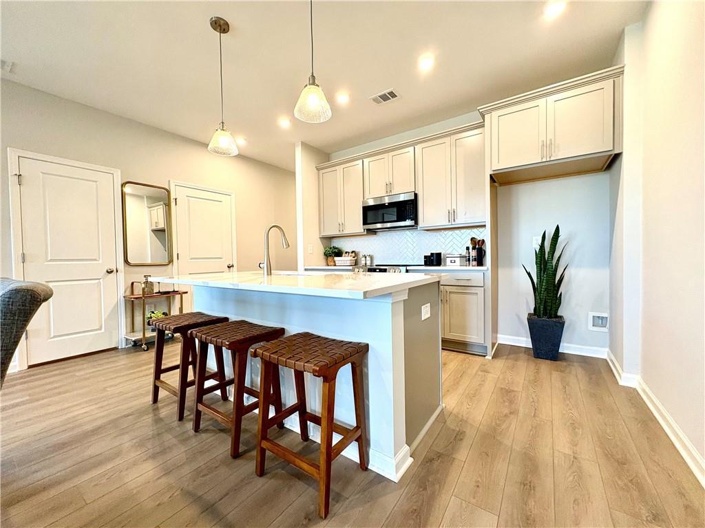 Modern open-concept kitchen with white shaker cabinets, quartz island, bar stools, and stainless appliances in Davidson Homes The Monroe A, Emerson, GA