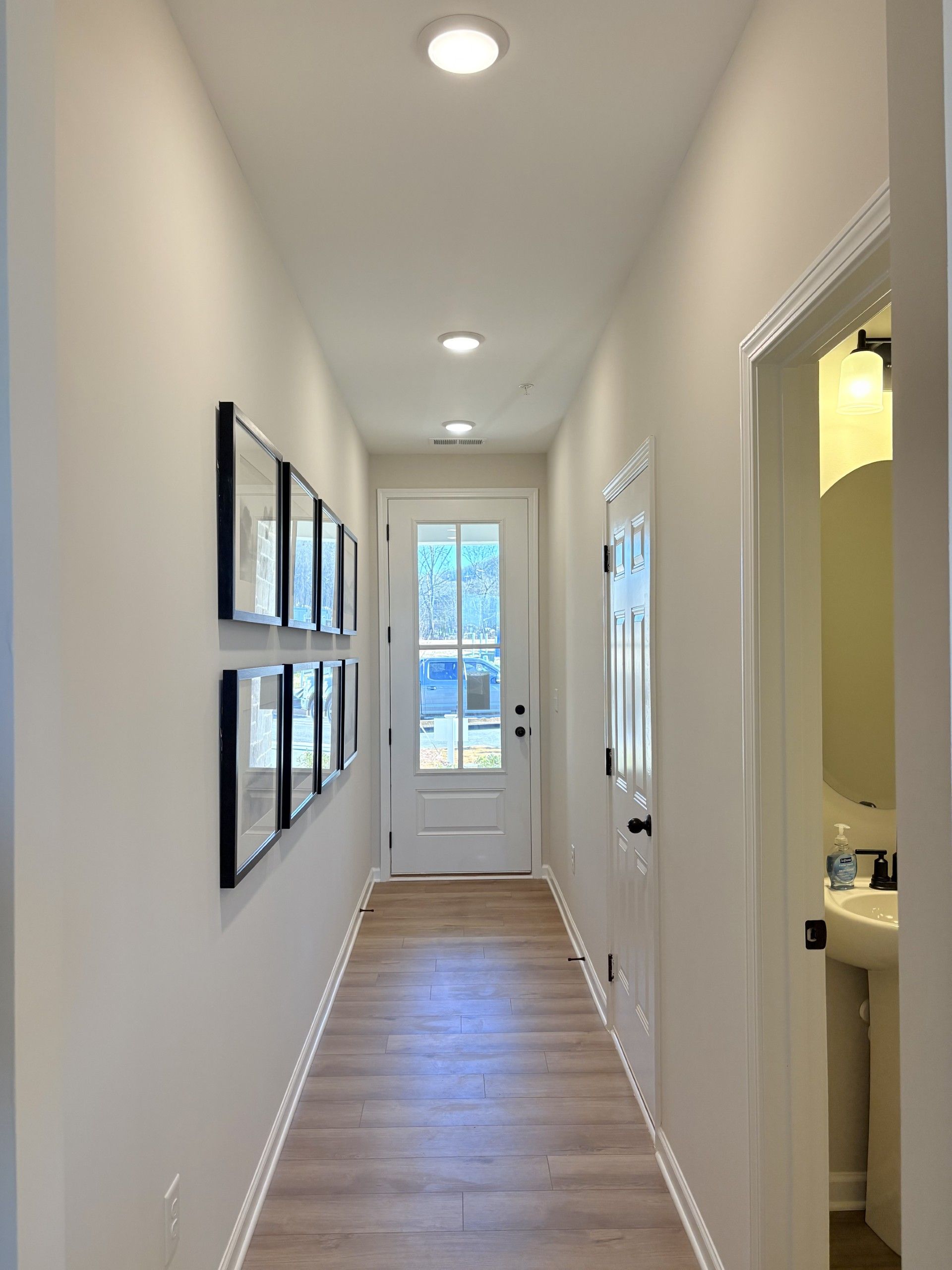 Spacious hallway in Hemingway Cumming GA home by Davidson Homes with light wood floors, gallery wall art and powder room