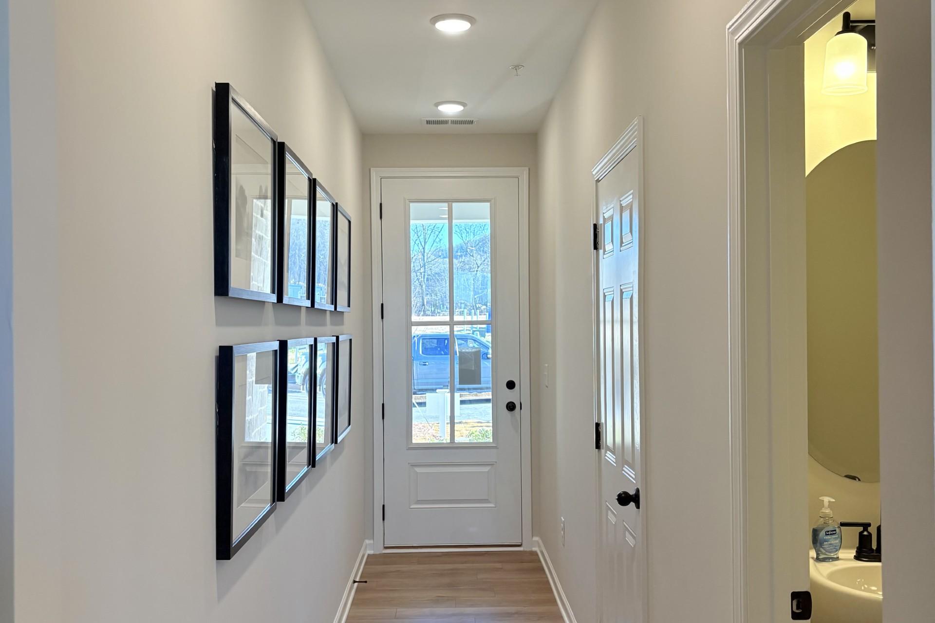 Spacious hallway in Hemingway Cumming GA home by Davidson Homes with light wood floors, gallery wall art and powder room