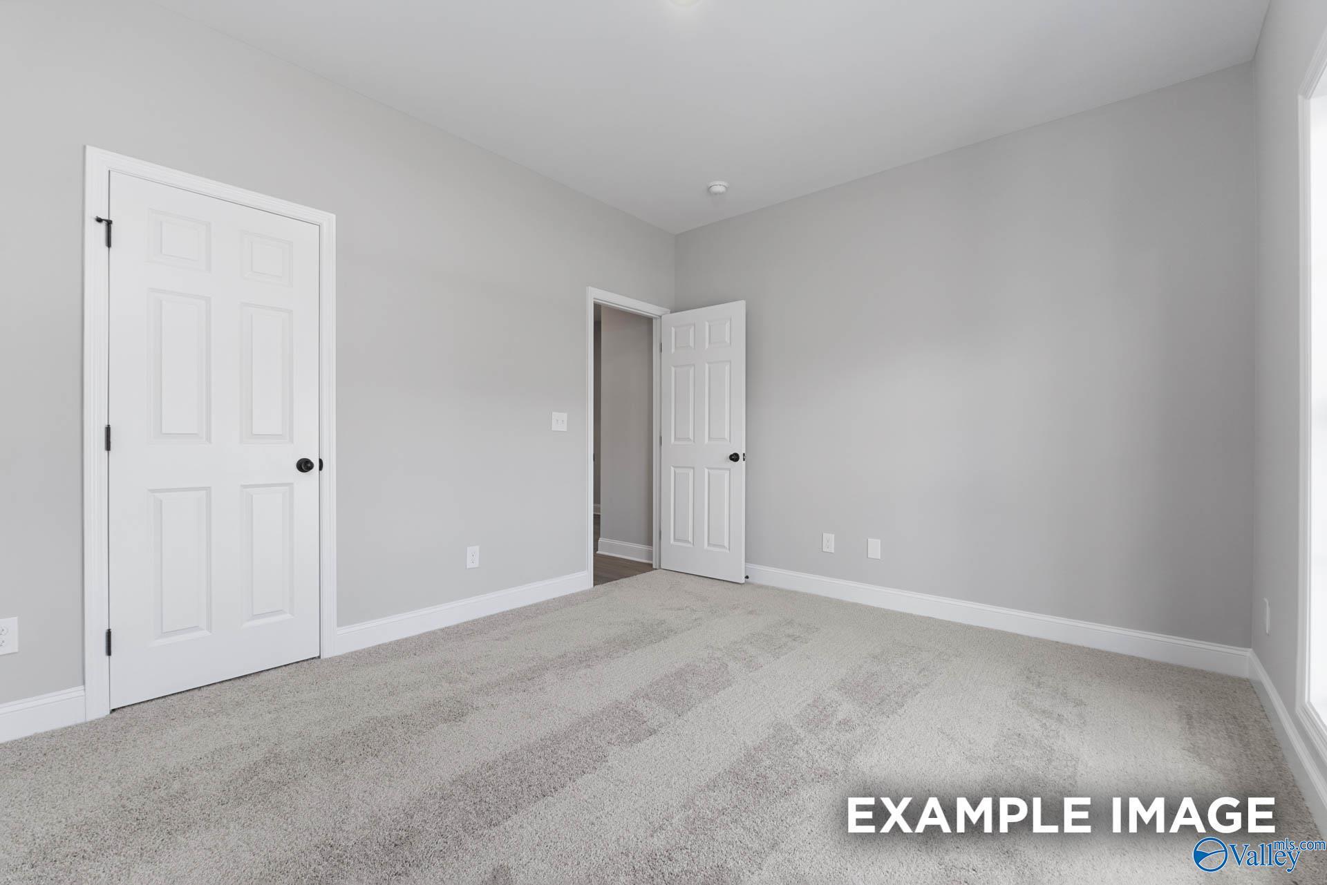 Bright secondary bedroom with gray walls, carpet flooring, and open bathroom door in The Daphne D, Meridianville, Alabama