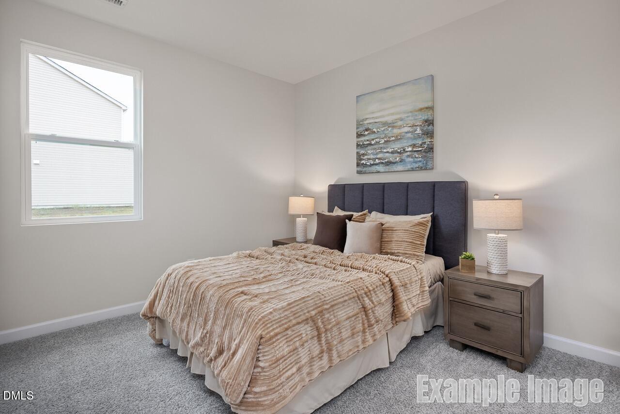 Cozy bedroom with beige quilted bedding, navy headboard, wood nightstands, lamps, and abstract seascape art in Davidson Homes The Carter C, Lillington, NC