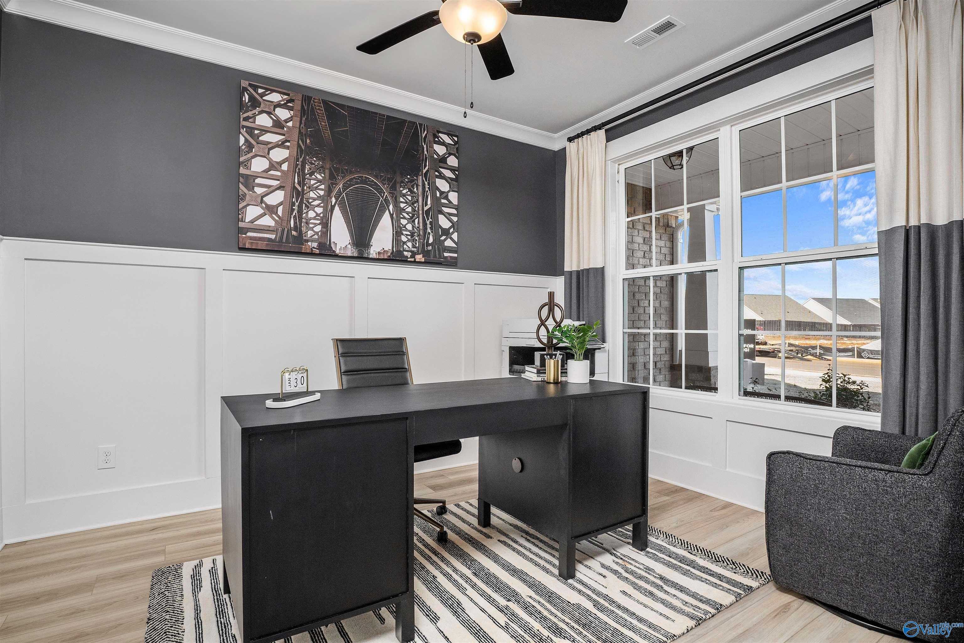 Modern home office with black desk, ceiling fan, large window, Eiffel-inspired art in Davidson Homes The Rockford B, Madison, AL