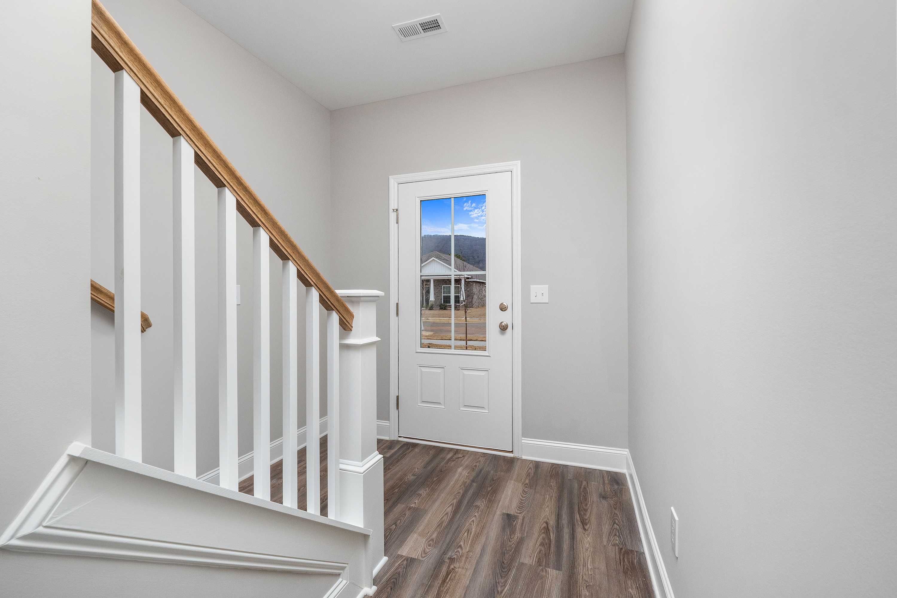 Spacious foyer in The Aiken two-story home with wooden staircase, white railings, hardwood floors, and glass-paneled entry door