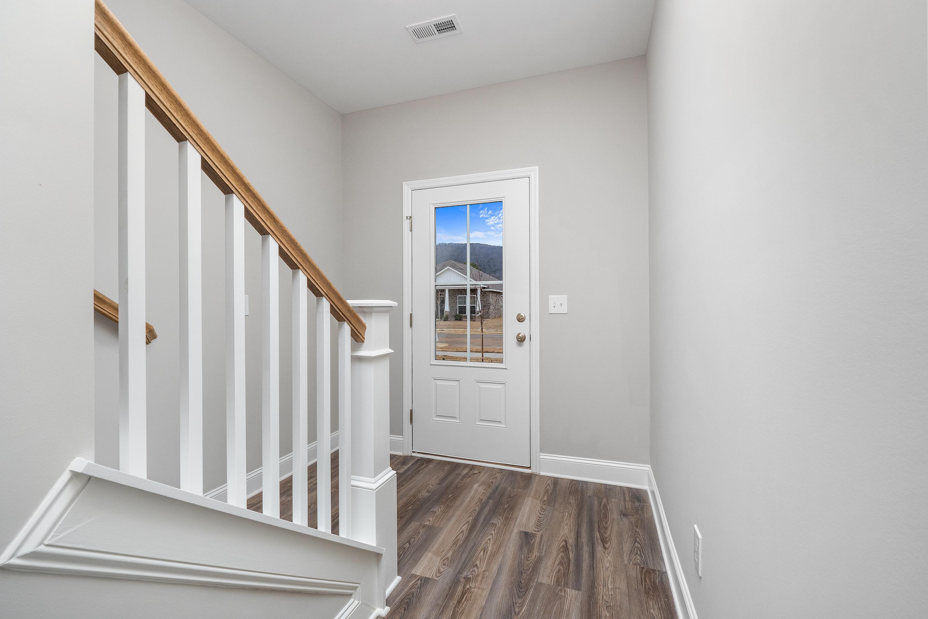 Spacious foyer in The Aiken two-story home with wooden staircase, white railings, hardwood floors, and glass-paneled entry door