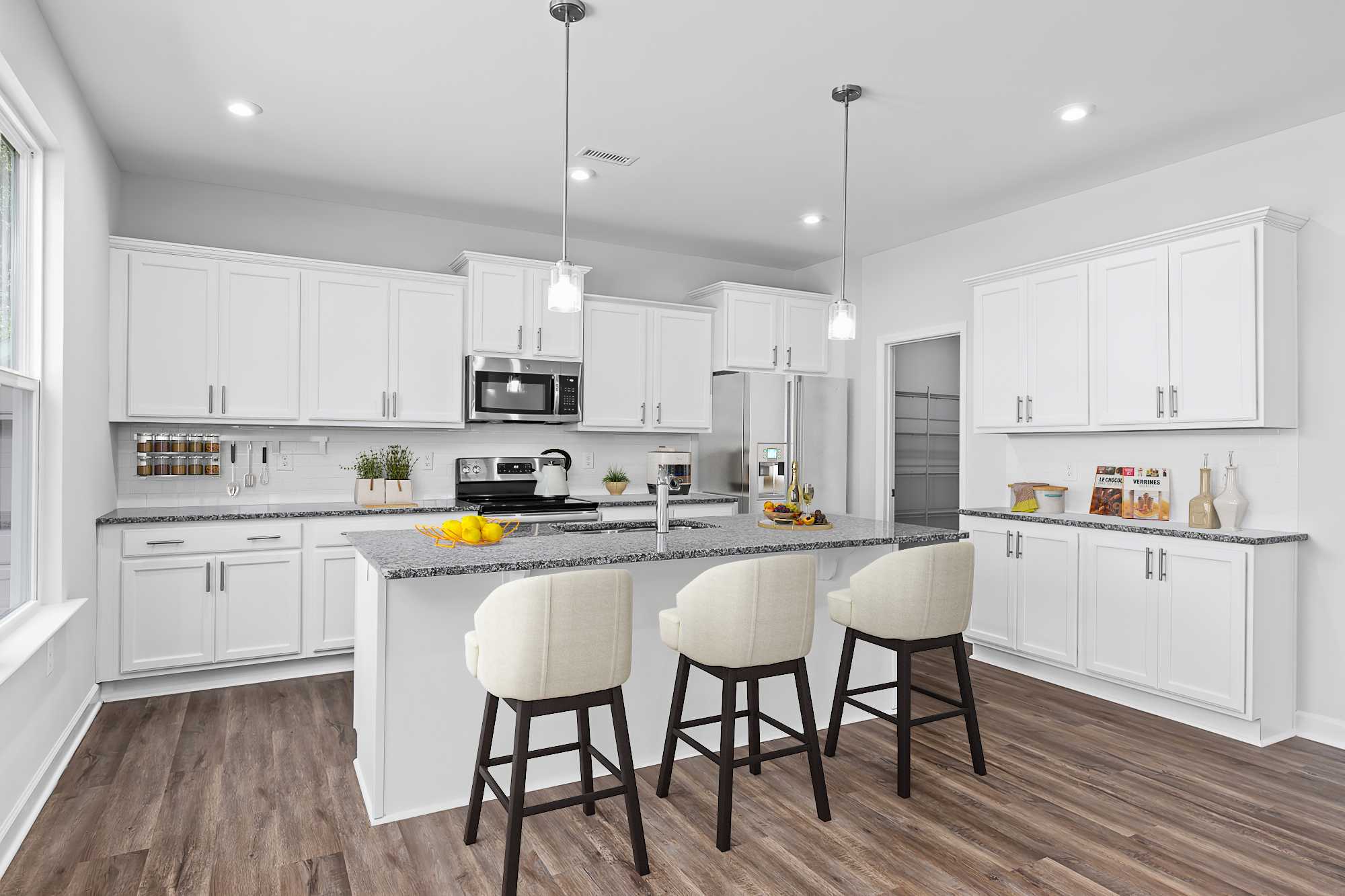 Spacious white kitchen at Enclave at Belmont in Belmont NC with large island, upholstered bar stools, hardwood floors, and pendant lights