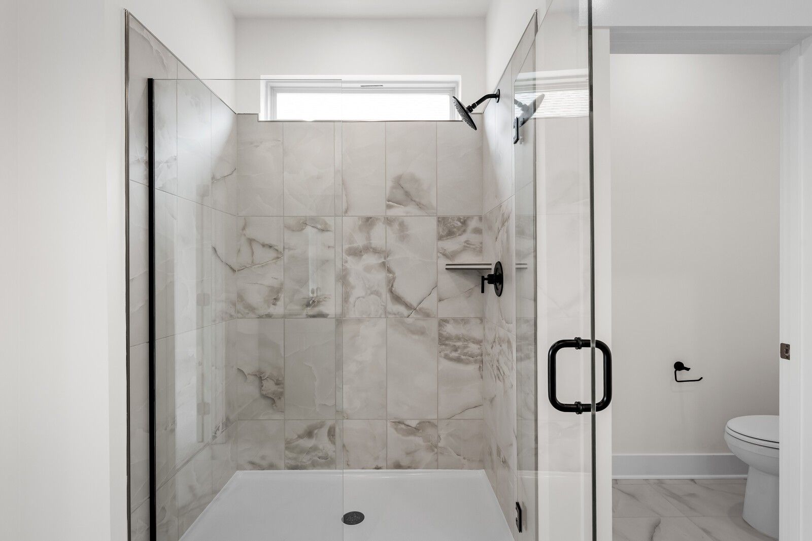 Modern walk-in shower with marble-look tile and glass door in a Davidson Homes floor plan at Woods Crossing, Gallatin.